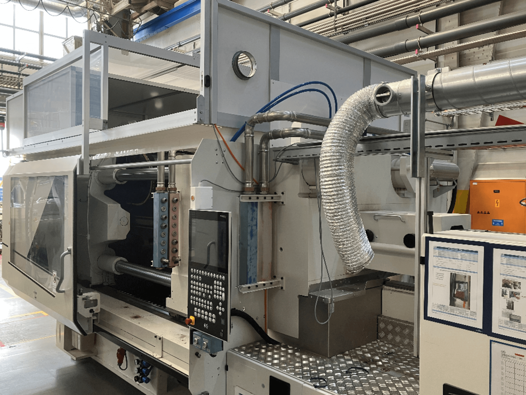 Industriële machine van Merk X, zijaanzicht met bedieningspaneel, leidingwerk en machineonderdelen in een fabrieksomgeving.