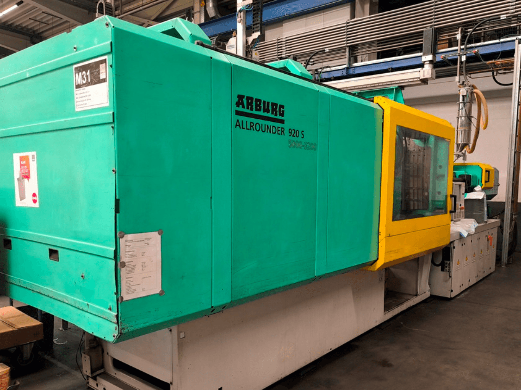 Arburg Allrounder 920 S spuitgietmachine in aquablauw en geel, zijaanzicht met bedieningspaneel en componenten.
