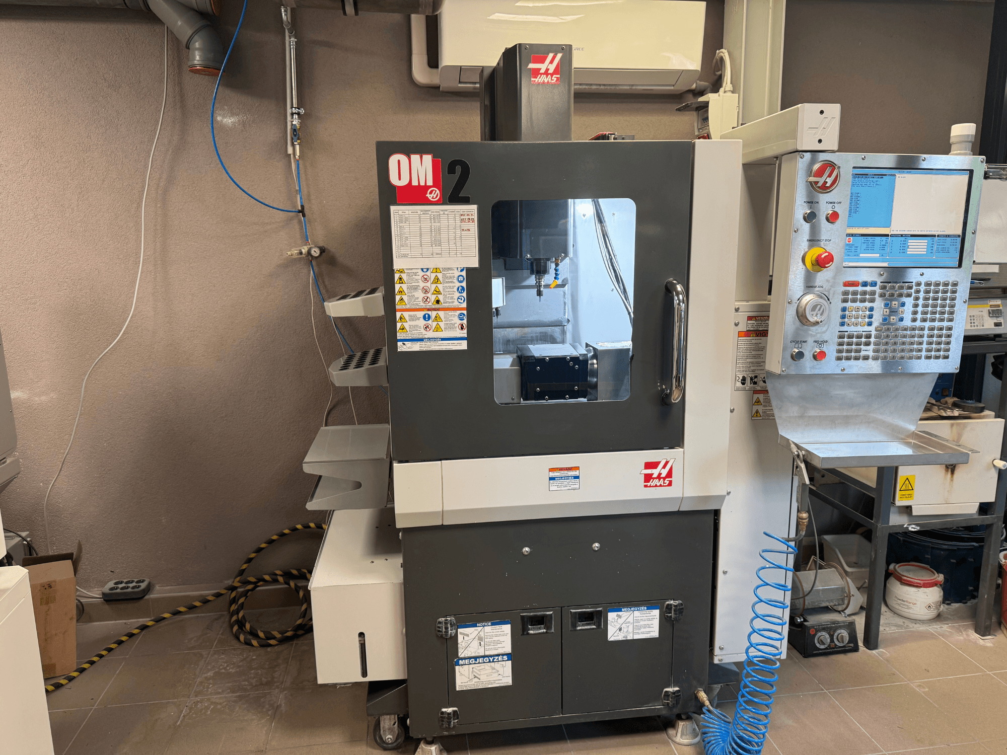 Haas OM-2 CNC machine, vooraanzicht, met bedieningspaneel, spindel en veiligheidslabels, opgesteld in een werkplaatsomgeving.