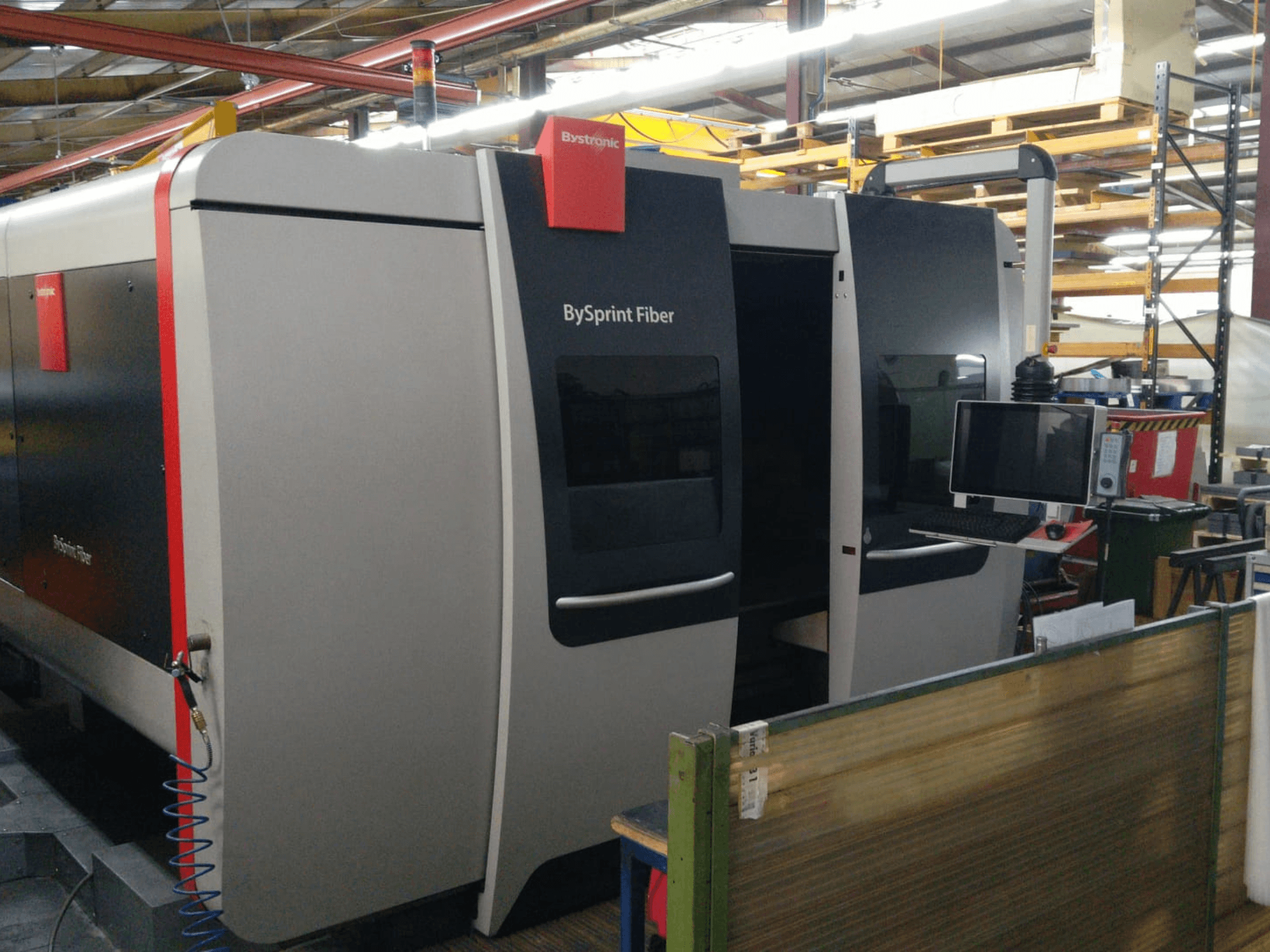 Bystronic BySprint fiberlasersnijder, vooraanzicht met bedieningspaneel, zichtbare details zijn onder andere twee deuren en een monitor aan de zijkant.