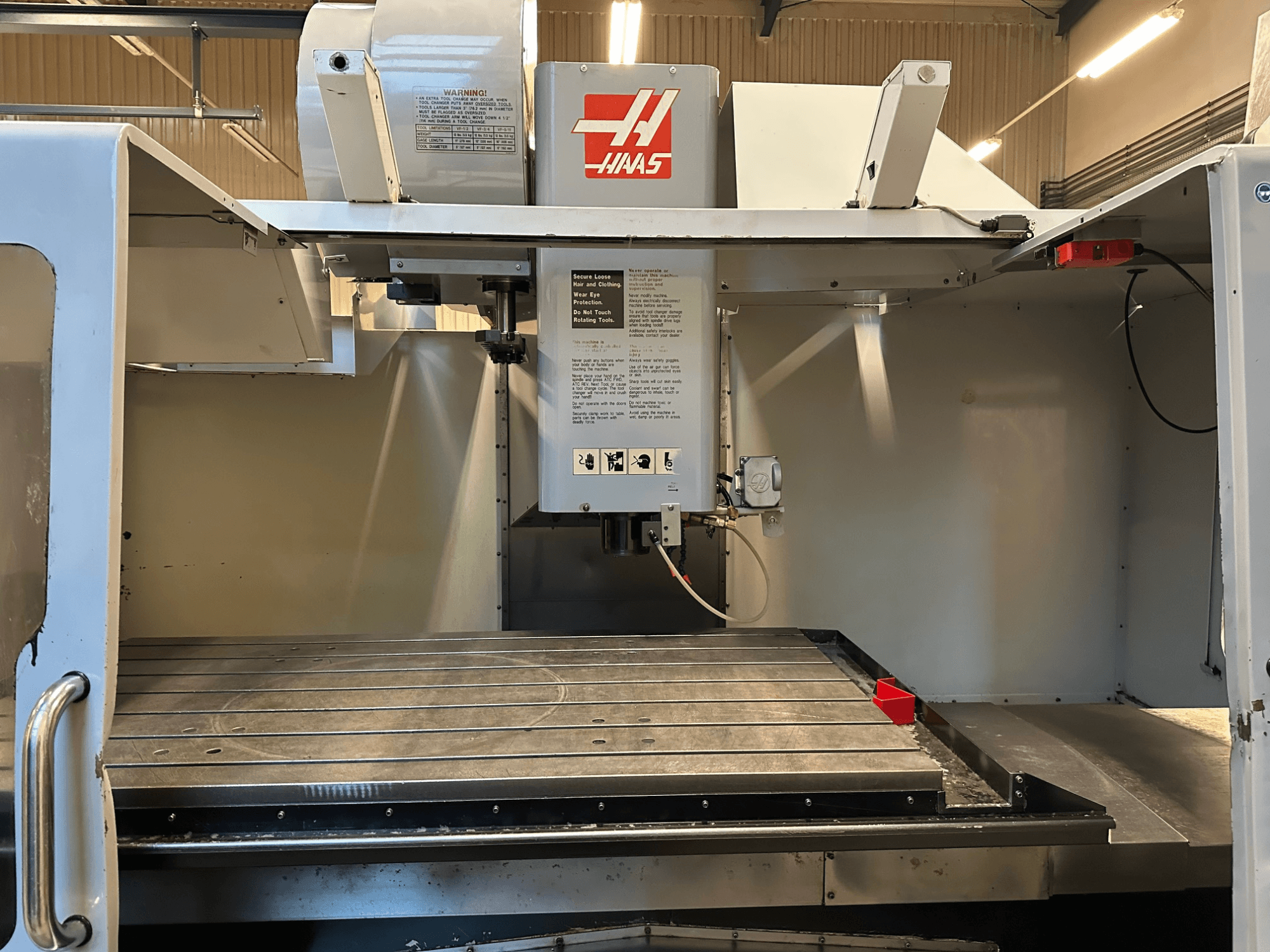 Haas CNC freesmachine, model VF-2, vooraanzicht met bedieningselementen, metalen werktafel en veiligheidslabel op het paneel.