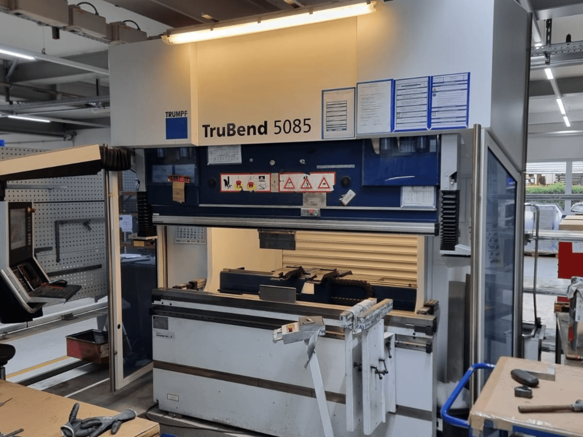 TRUMPF TruBend 5085 buigmachine, vooraanzicht, met bedieningspaneel, bedieningsstation en veiligheidswaarschuwingen in de werkplaats.