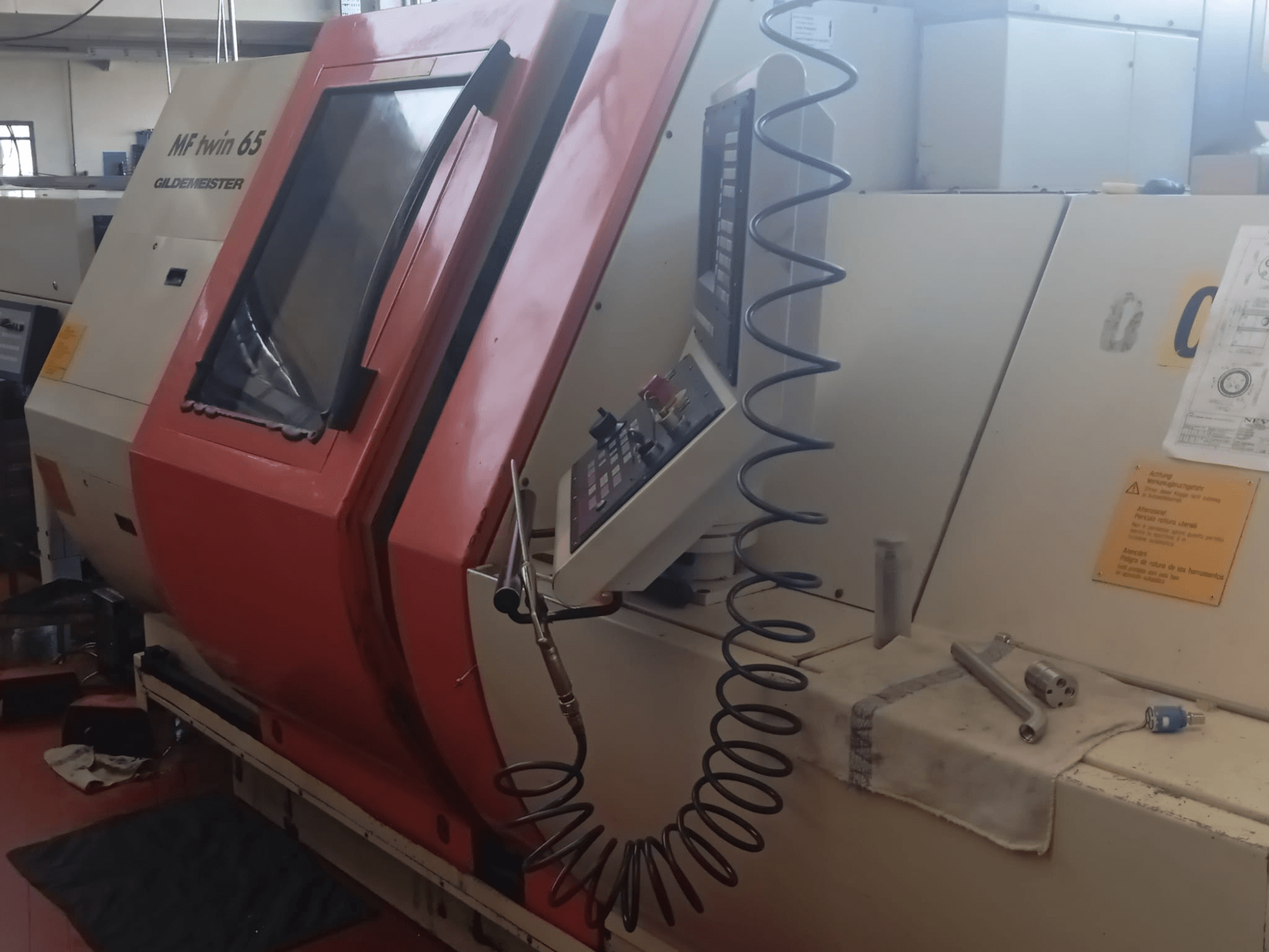 Oranje en witte MF twin 65 Gliedemeister machine, vooraanzicht, met bedieningspaneel en gereedschap op een doek.