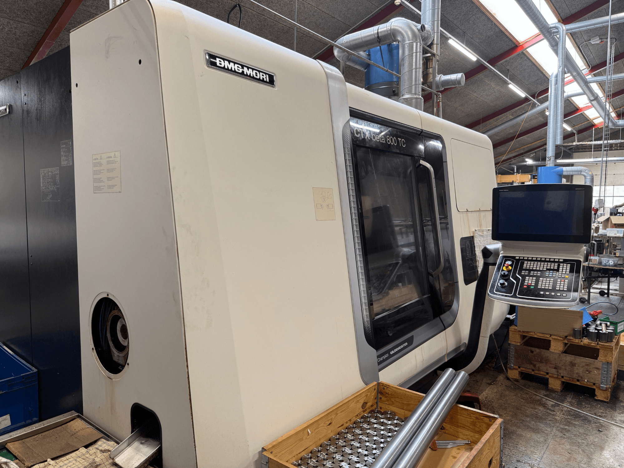 DMM-MORI CTX beta 800 TC machine, vooraanzicht, met bedieningspaneel, gereedschap en metalen staven op een houten pallet.