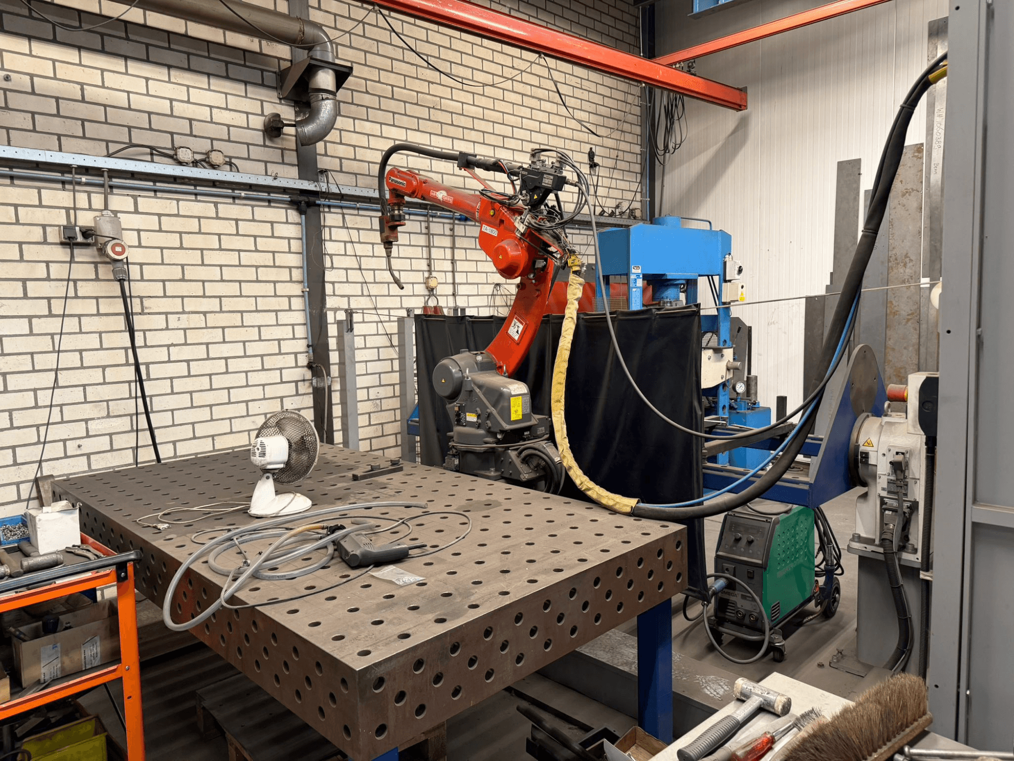 Vooraanzicht van een PANASONIC TA-1800 lasrobot op een werkstation, met een ventilator en lasapparatuur zichtbaar.