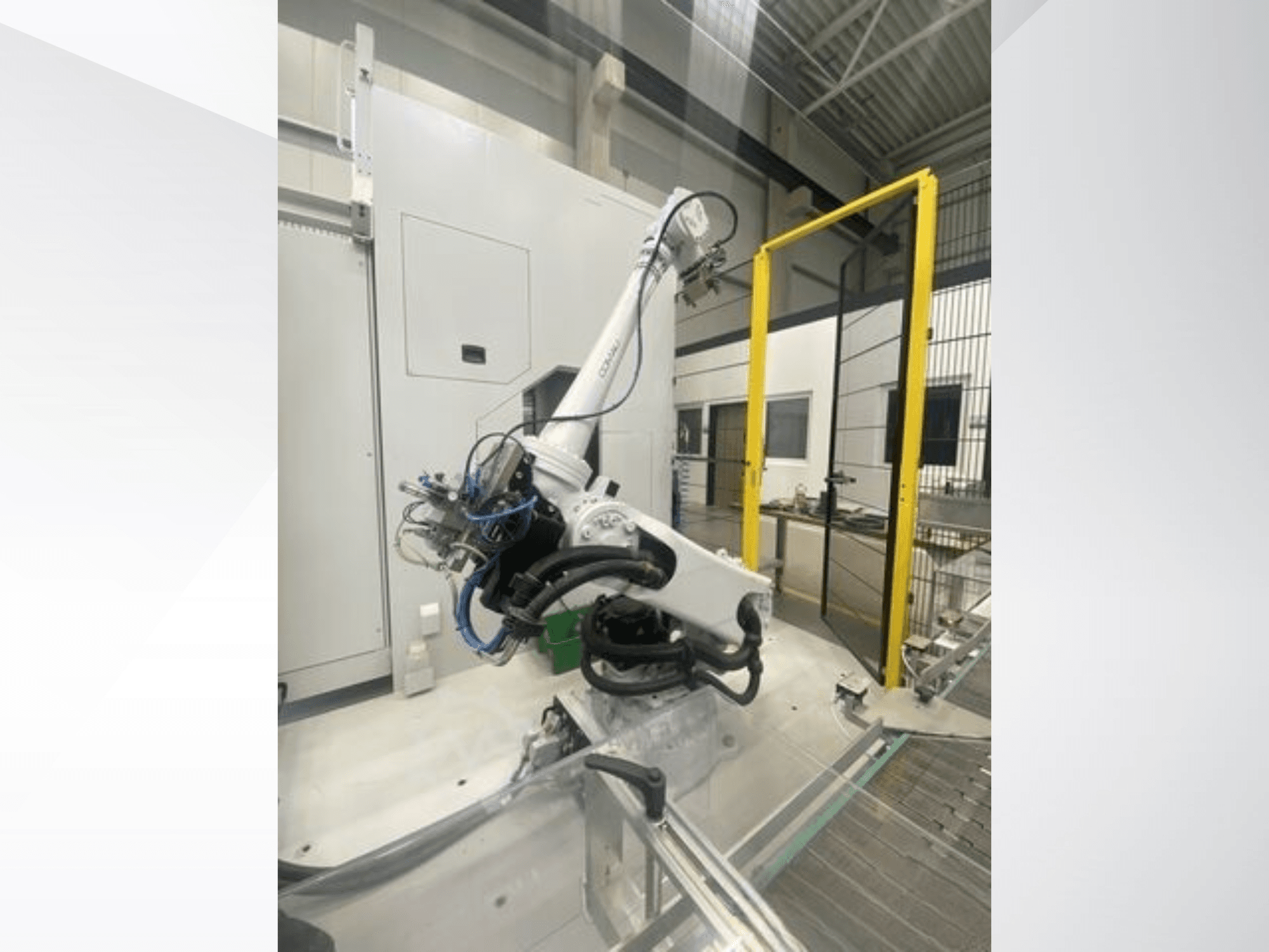 COMAU Smart NJ 40-2.5 robotarm in zijaanzicht, met kabels en een geel veiligheidshek in een fabrieksomgeving.