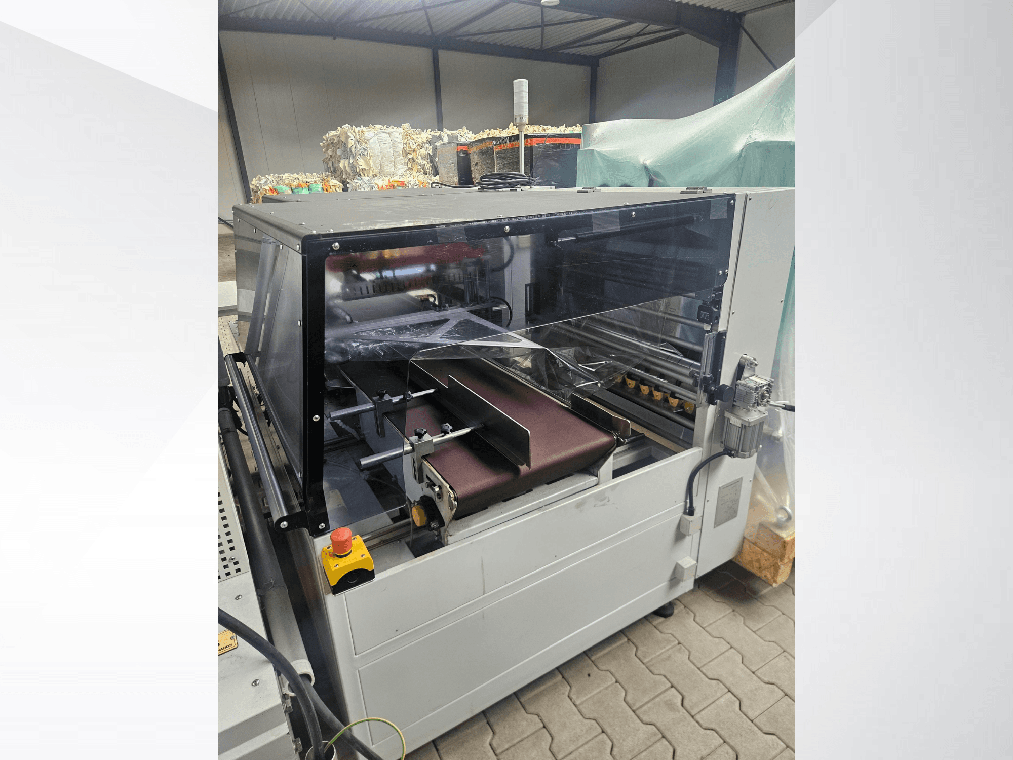AMTEC Speed Shrink 40 PRO-machine, vooraanzicht, met een kunststofverwerkingsmechanisme met een doorzichtige veiligheidsafdekking en een transportband.