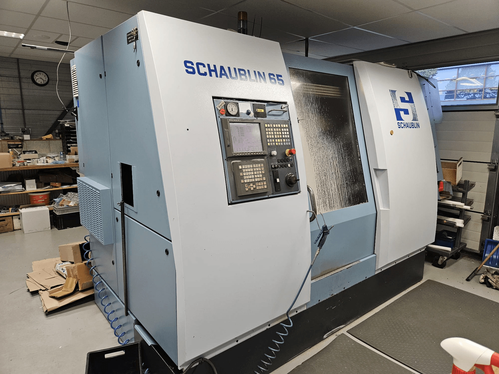 SCHAUBLIN 65 CNC machine, zijaanzicht, met bedieningspaneel, blauwe en grijze behuizing en zichtbaar koelsysteem.