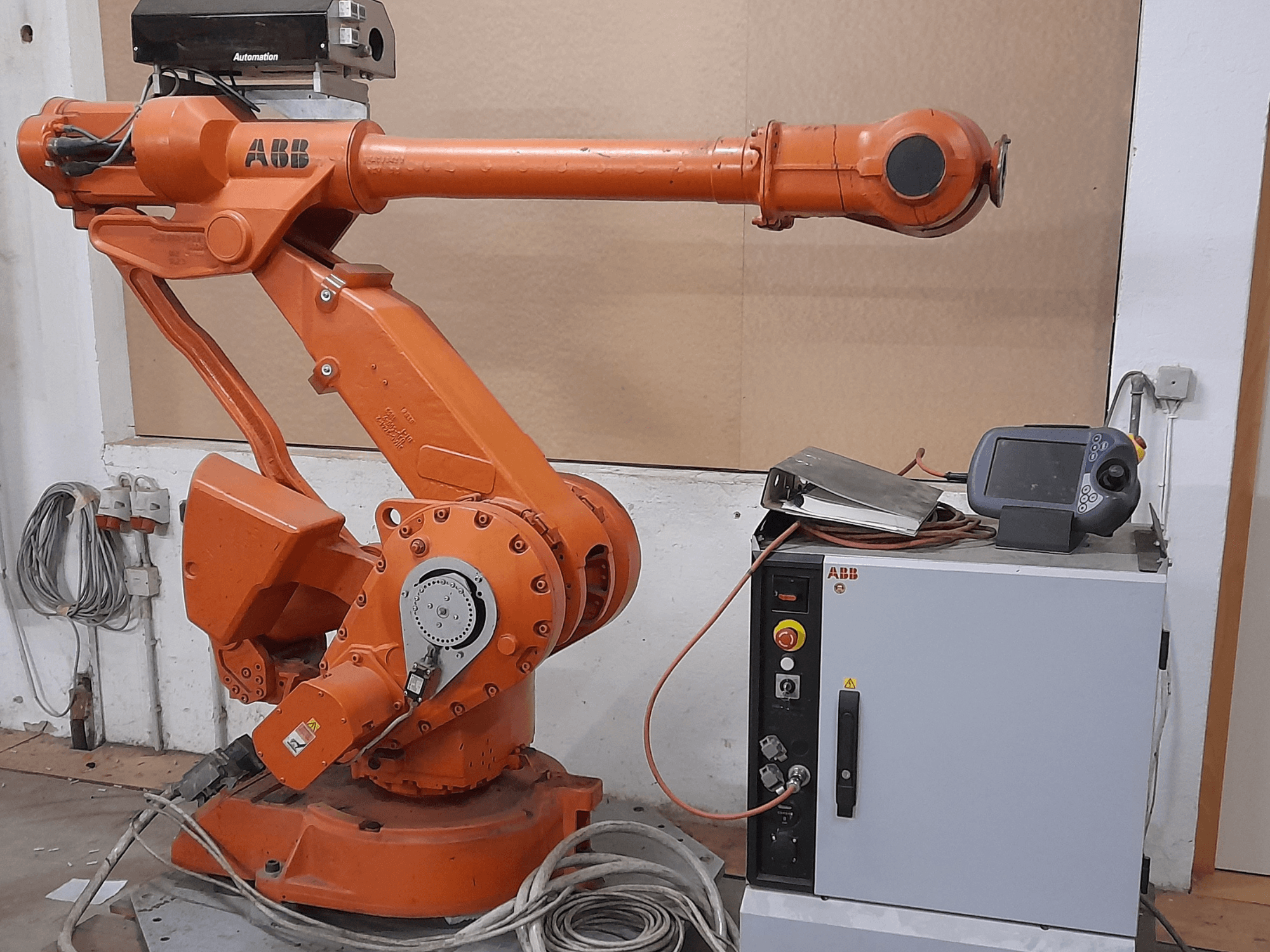 Oranje ABB robotarm met bedieningspaneel, vooraanzicht, met kabels en automatiseringsapparatuur.