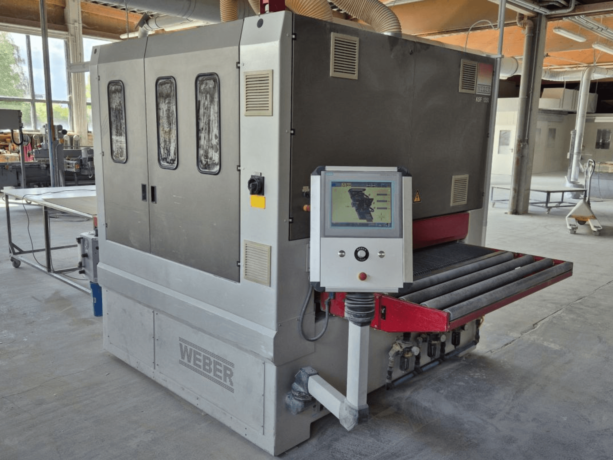 WEBER KSF-3-1350 bandschuurmachine, zijaanzicht met bedieningselementen, vermogenspaneel en schuurband. Industriële omgeving met machines zichtbaar.