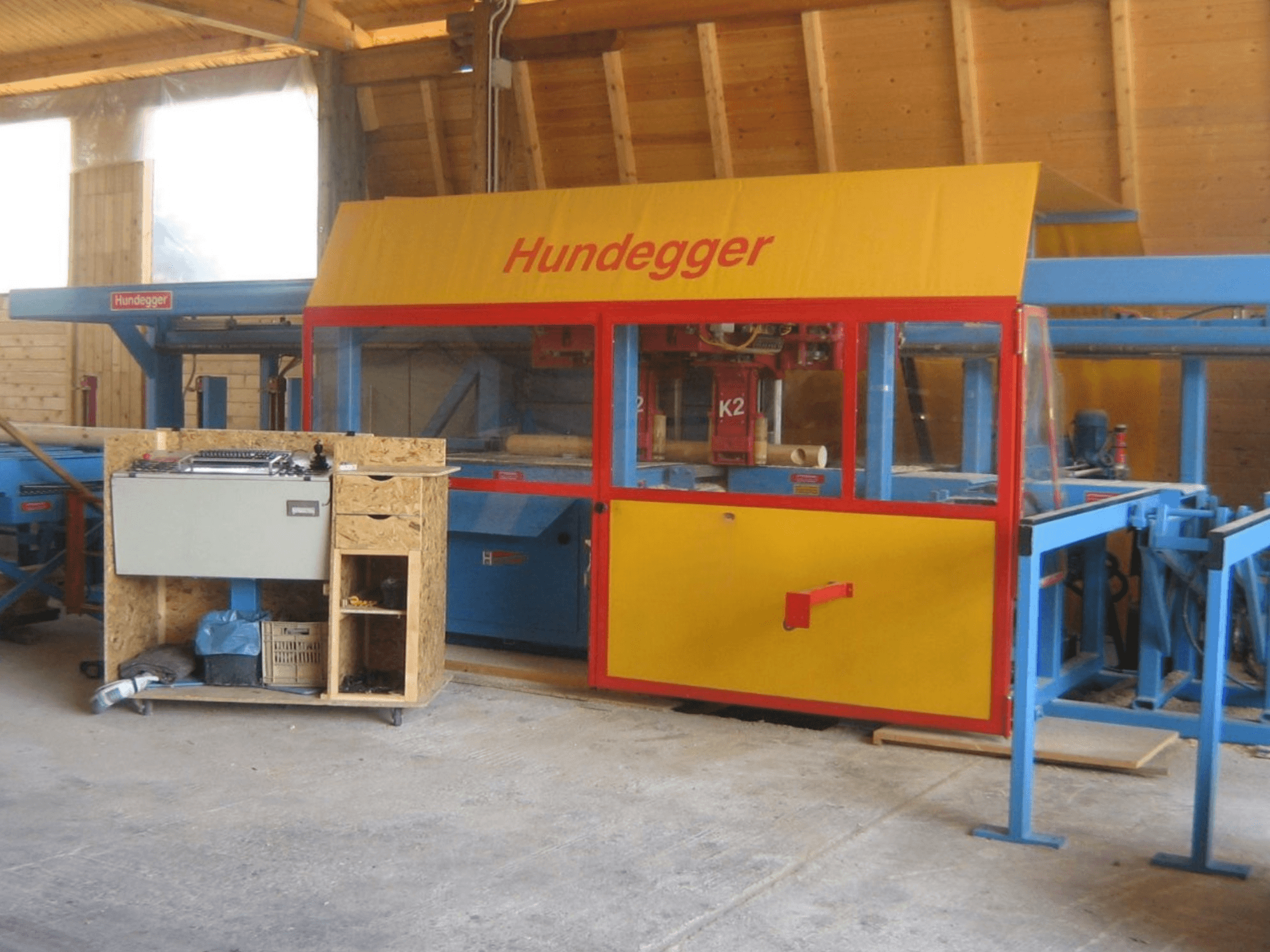 CNC houtbewerkingscentrum HUNDEGGER K2 4 assi in een werkplaats, vooraanzicht met geel en blauw ontwerp en werktafel.