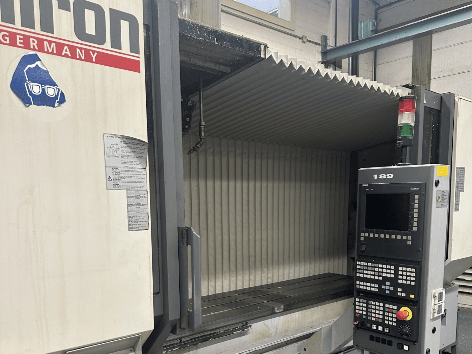 Alt-tekst: Vooraanzicht van een Hermle CNC machine met een bedieningspaneel met knoppen en een display, met een open werkgebied.