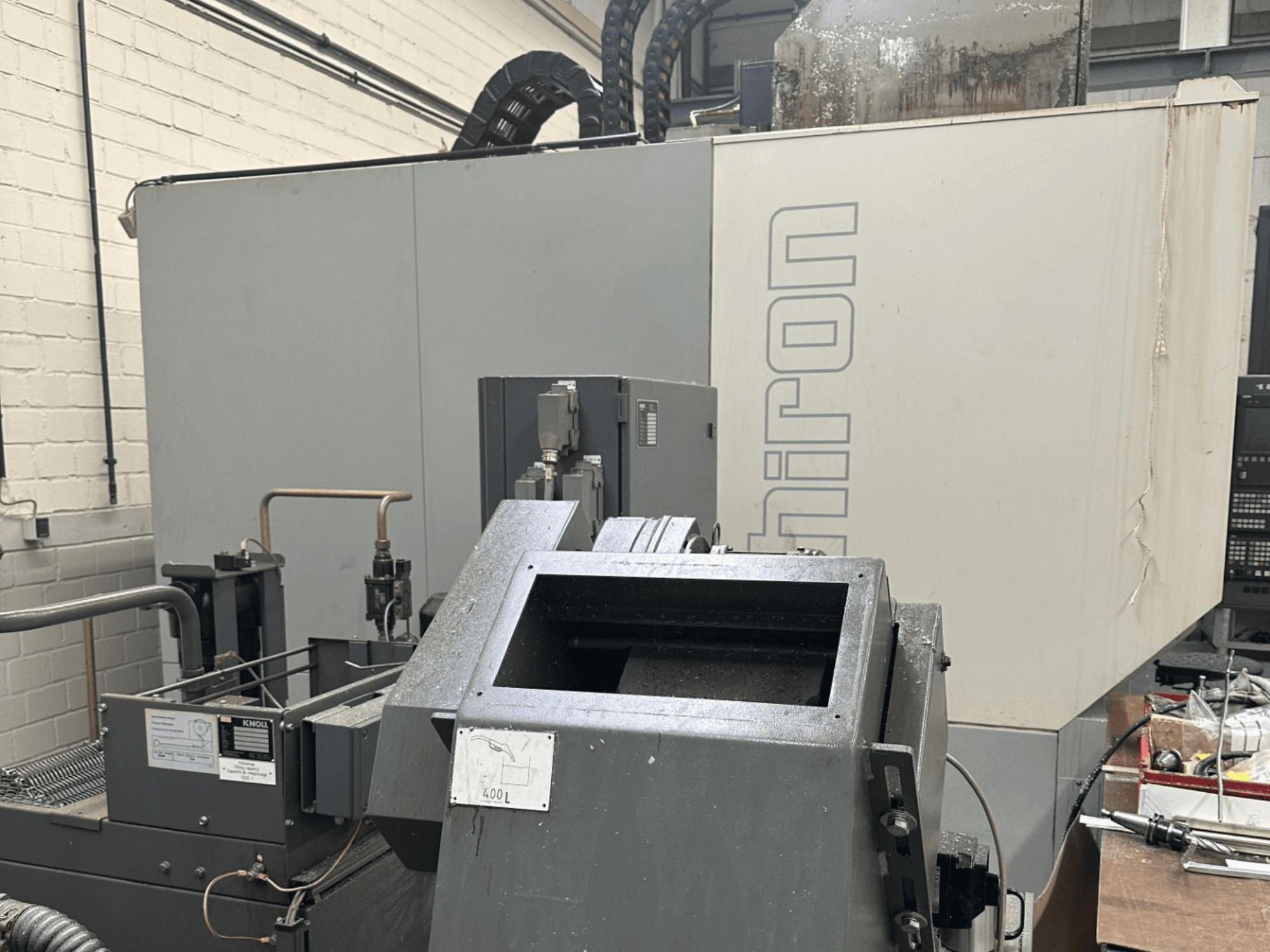 Merk: Chiron; vooraanzicht van industriële CNC-machine met grijze buitenkant, bedieningspaneel zichtbaar en machineonderdelen in beeld.