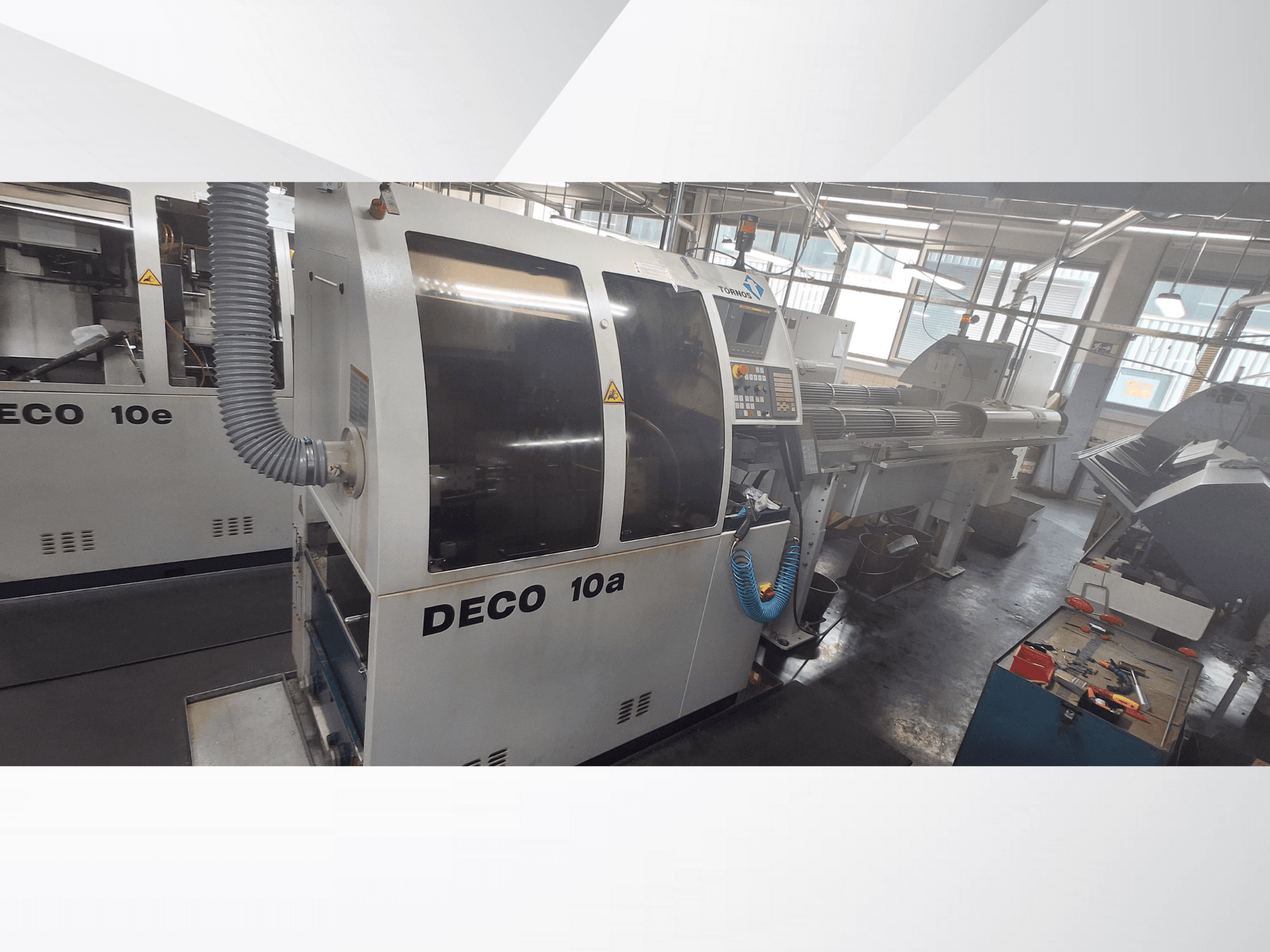 DECO 10a CNC machine in een werkplaats, met vooraanzicht, bedieningspaneel en uitlaatsysteem. Robuuste constructie en precisiegereedschap.