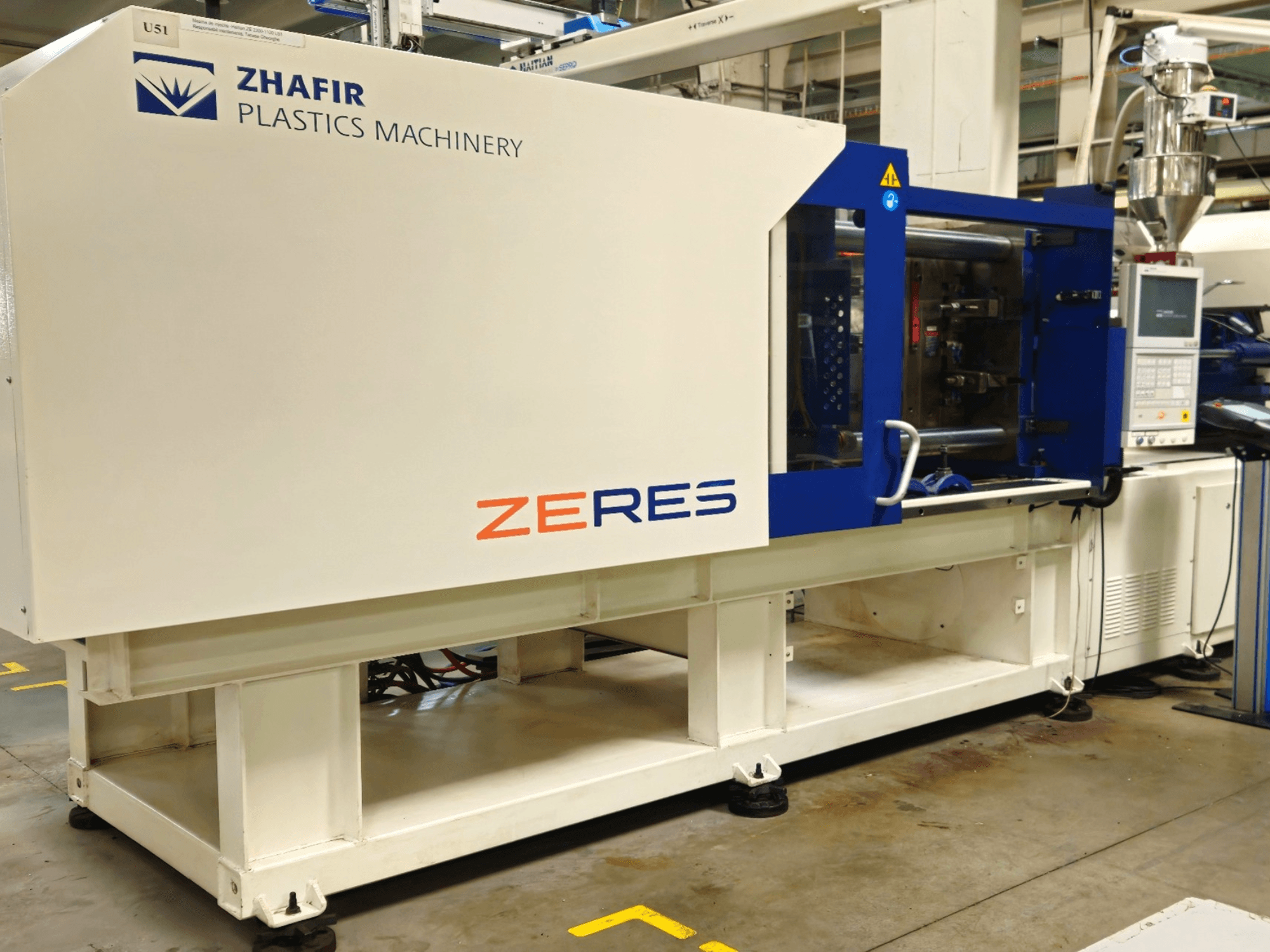 Zhafir Zeres kunststof spuitgietmachine, zijaanzicht, met bedieningspaneel, trechter en gestroomlijnd wit/blauw ontwerp.