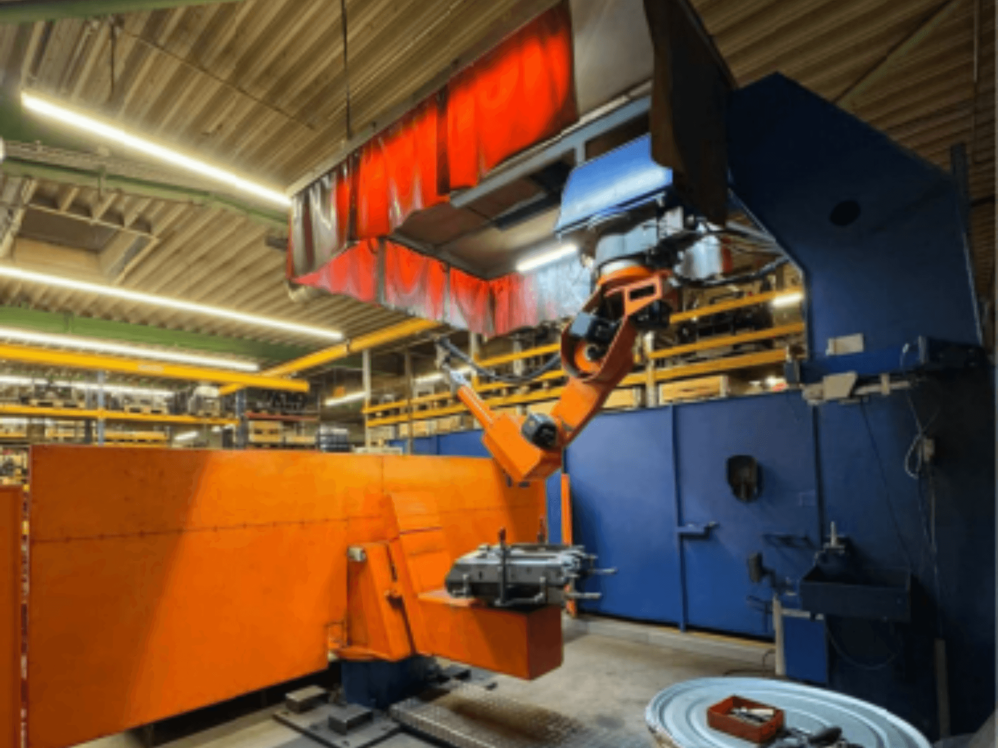 CLOOS Romat 350 e lasrobot in een industriële omgeving, vooraanzicht met oranje arm, die een werkstuk vasthoudt onder een gordijn.