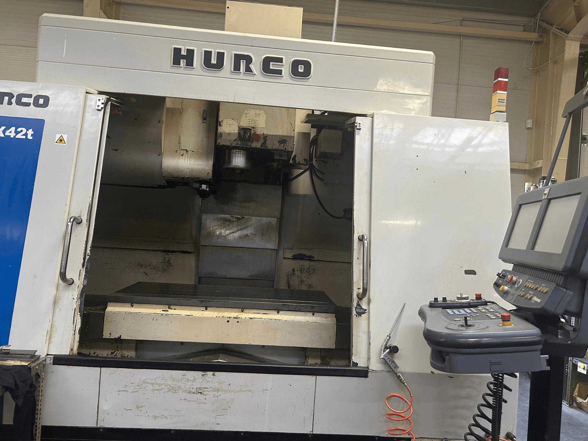 Hurco VMX42T CNC freesmachine in vooraanzicht, met een open werkruimte en bedieningspaneel met knoppen en display.