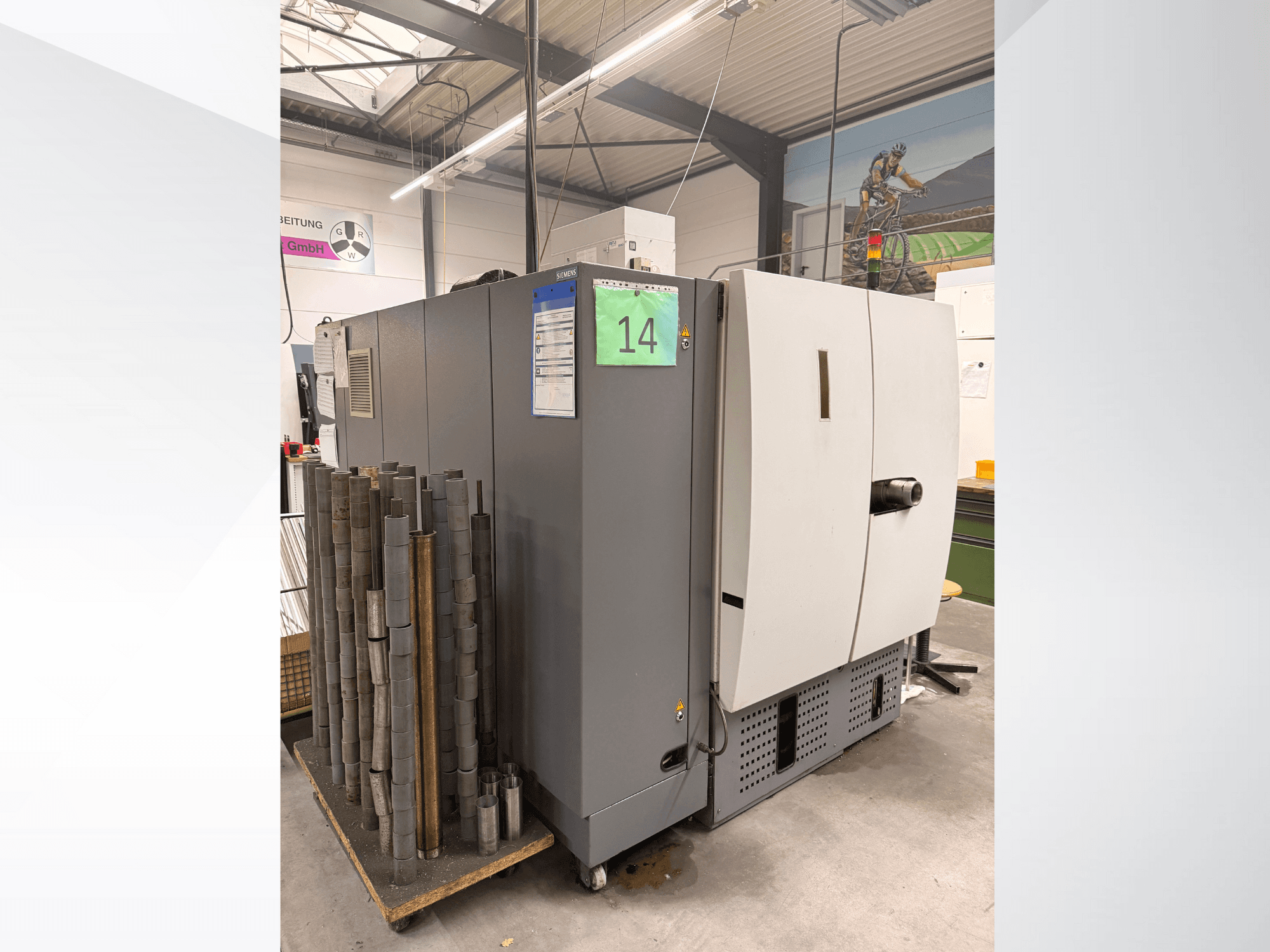 Grijze industriële machine van Siemens, zijaanzicht, met voorraad cilindrische metalen stukken ernaast en apparatuurlabels zichtbaar.