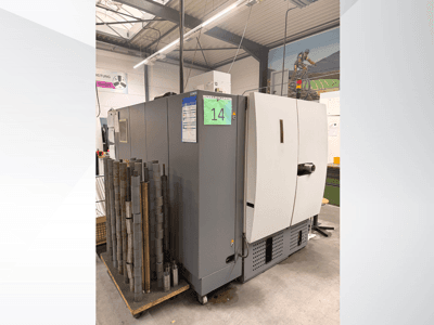 Grijze industriële machine van Siemens, zijaanzicht, met voorraad cilindrische metalen stukken ernaast en apparatuurlabels zichtbaar.
