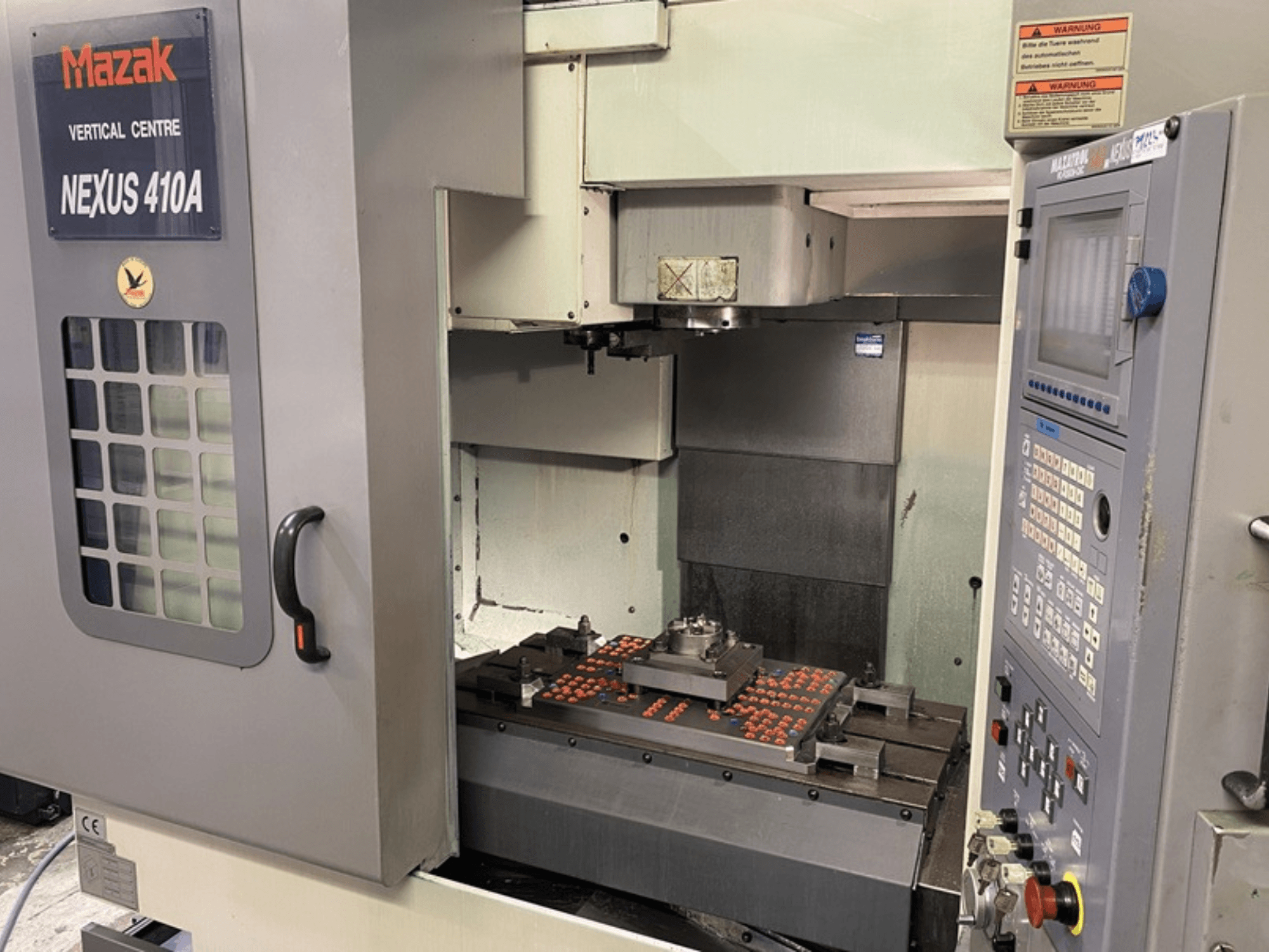 Mazak VCN410 verticaal bewerkingscentrum, vooraanzicht met bedieningspaneel en machine-interieur met gemonteerd werkstuk.