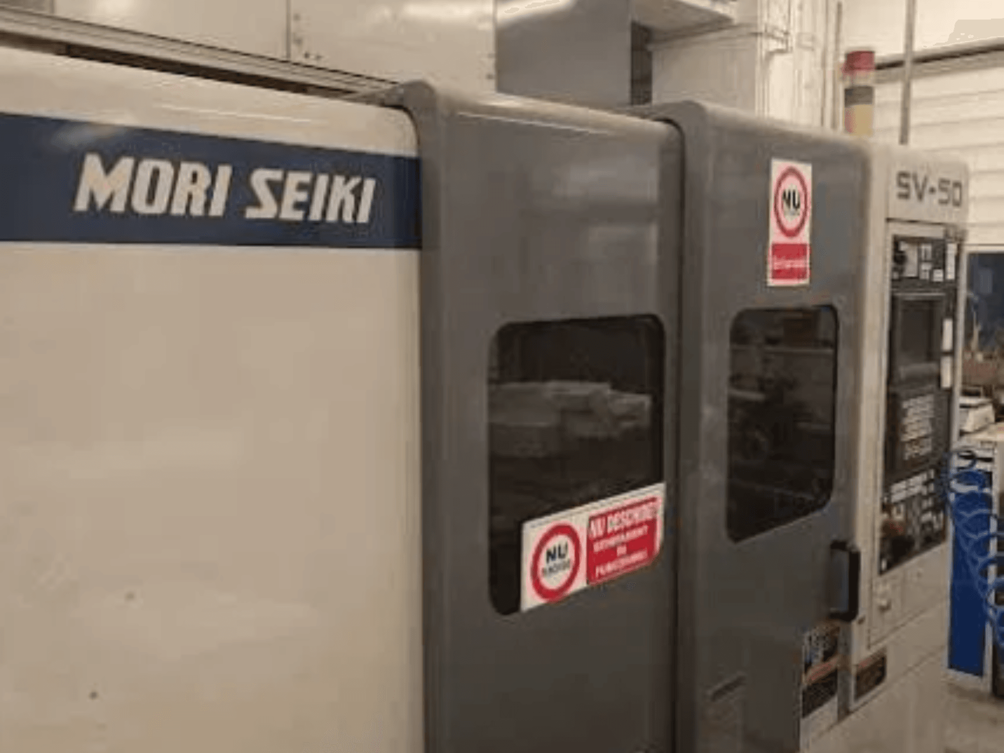 MORI SEIKI SV-50 CNC machine, zijaanzicht; voorzien van bedieningspaneel en waarschuwingsstickers.
