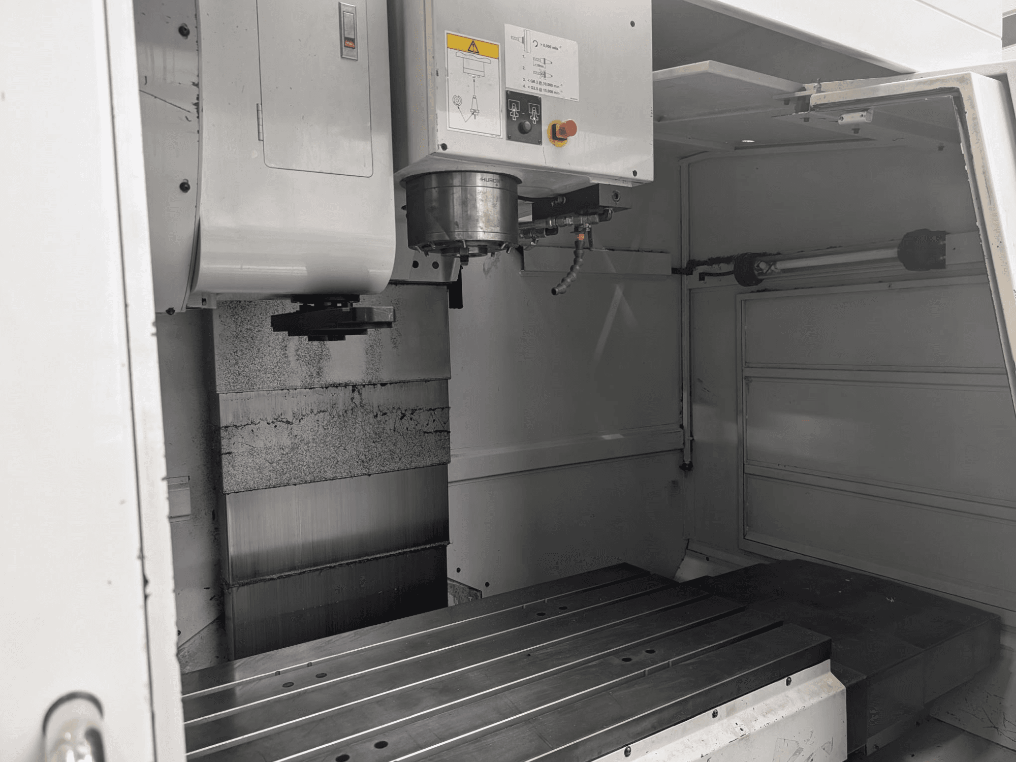 Binnenzicht van een CNC freesmachine met een grote metalen werktafel en spindelmotor, met gedetailleerde onderdelen en bedieningspaneel.