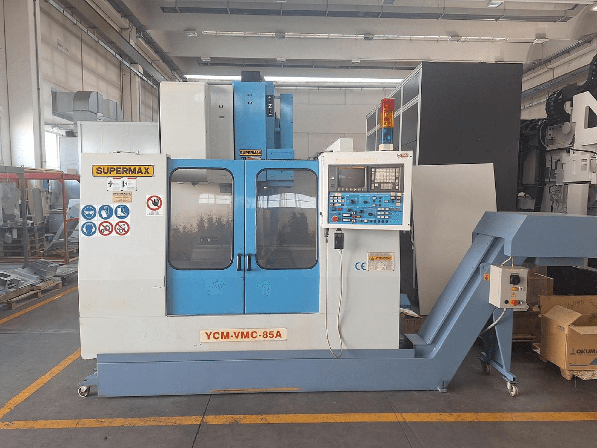 Verticaal bewerkingscentrum SUPERMAX YCM-VMC-85A in een fabriek, met bedieningspaneel en veiligheidsstickers, vooraanzicht.