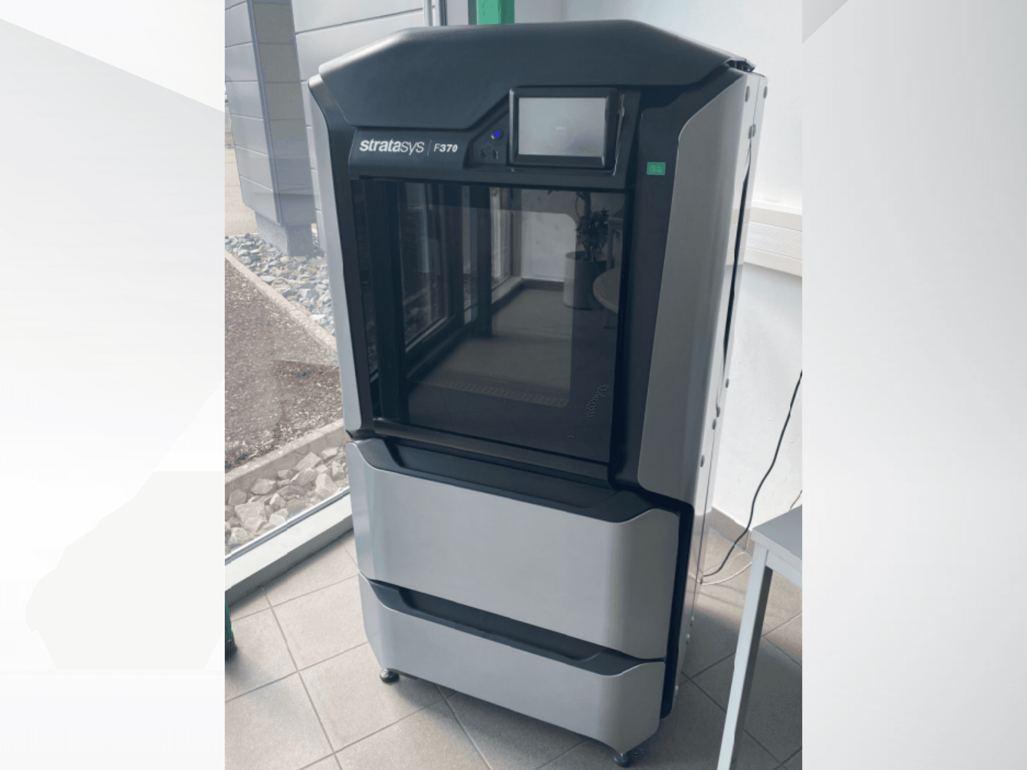 Stratasys F370 kunststof 3D printer, vooraanzicht, met een gestroomlijnd zwart en grijs ontwerp en een touchscreen display.
