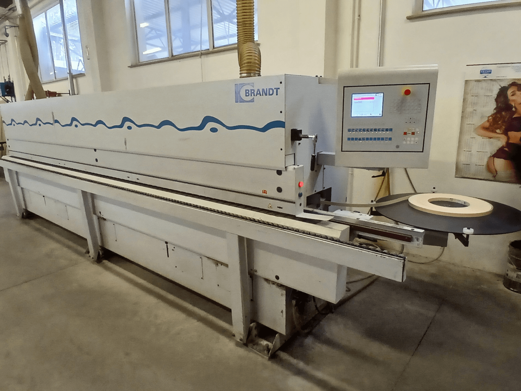 Brandt kantenaanlijmmachine, zijaanzicht, met een bedieningspaneel en een rol tape op de invoertafel.