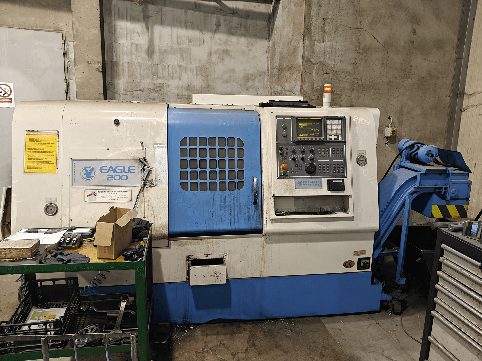 Eagle 200 CNC machine, vooraanzicht met bedieningspaneel, diverse gereedschappen op een groene kar. Zichtbare slijtage en bedrijfslampjes.