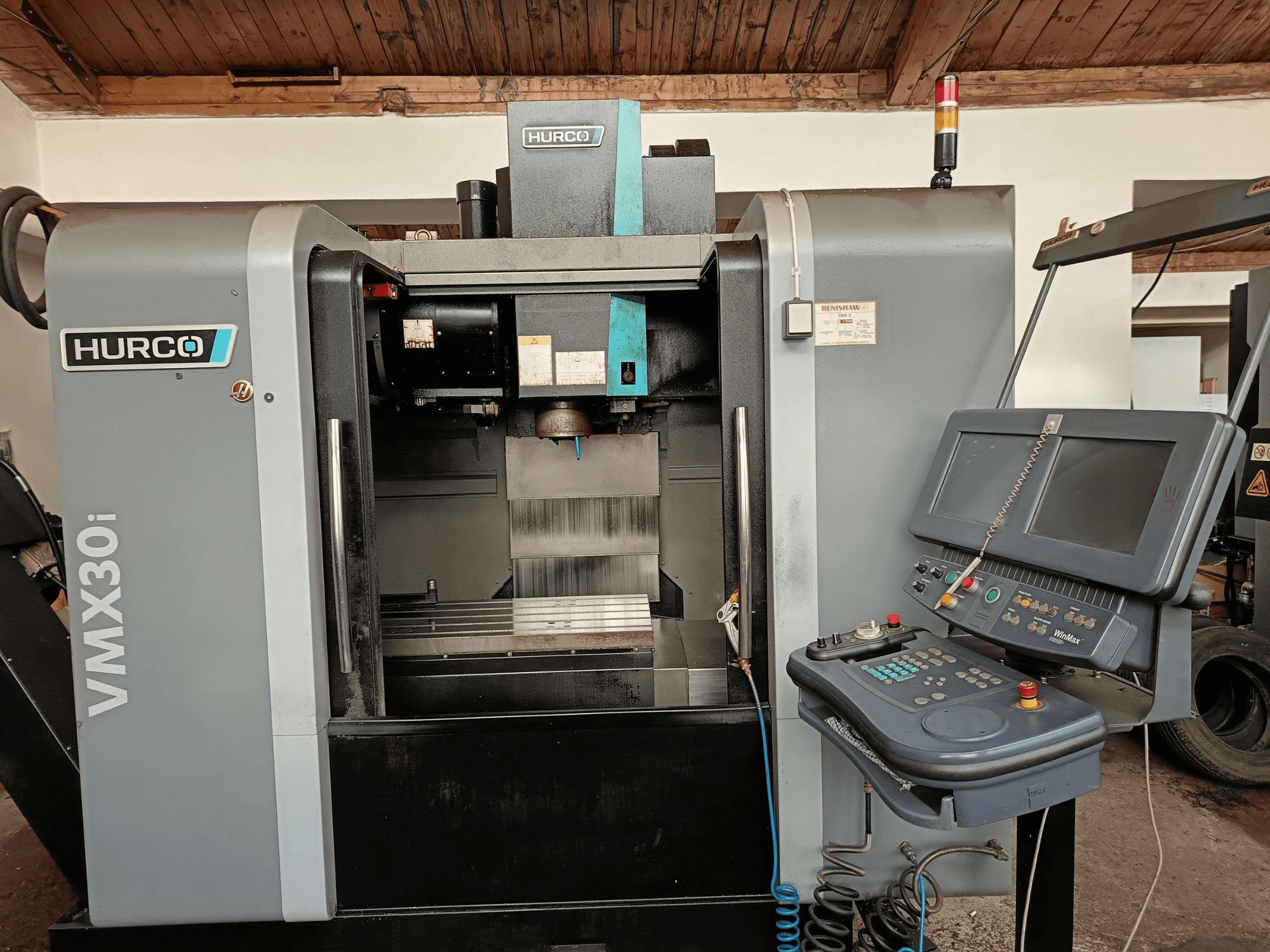 HURCO VMX30i bewerkingscentrum in vooraanzicht, met bedieningspaneel met knoppen en monitor, metalen werkgebied en waarschuwingslicht.