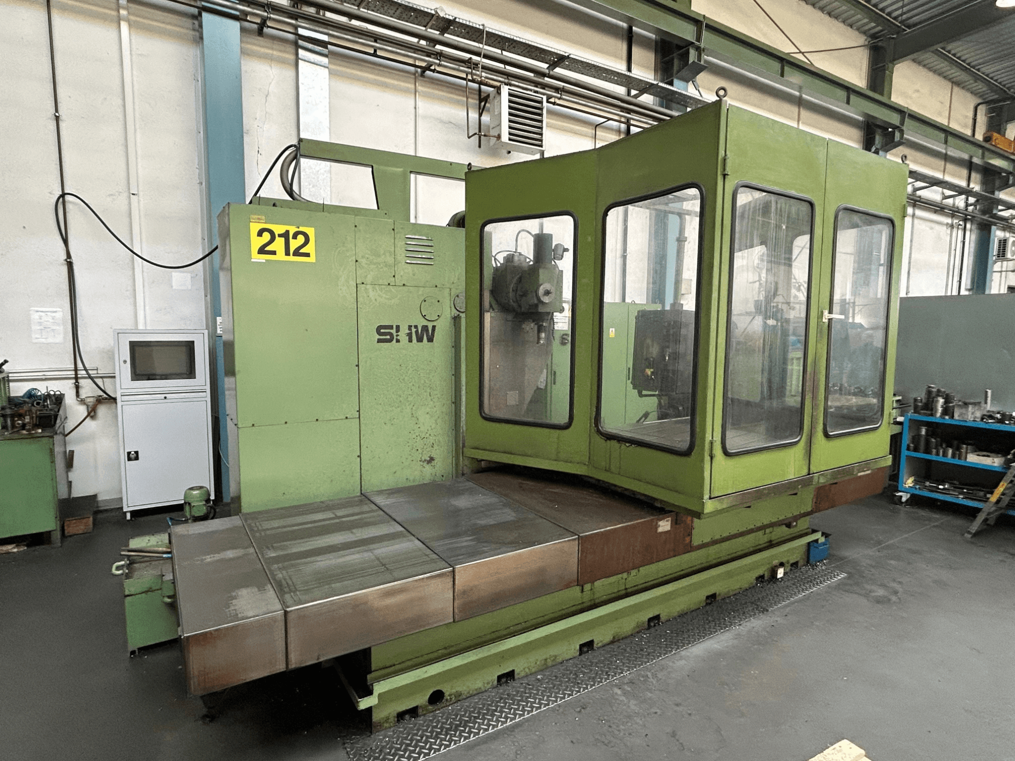 SHW UF-5 verticaal bewerkingscentrum in groen, vooraanzicht met bedieningspaneel, glazen behuizing en metalen werktafel.