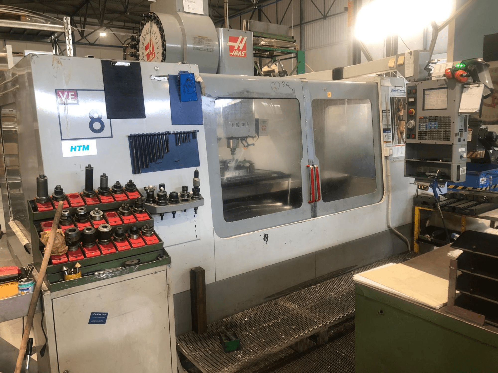 Haas CNC machine in een werkplaats, vooraanzicht; toont gereedschappen en bedieningselementen, met zichtbare modeldetails en georganiseerde gereedschapshouders.