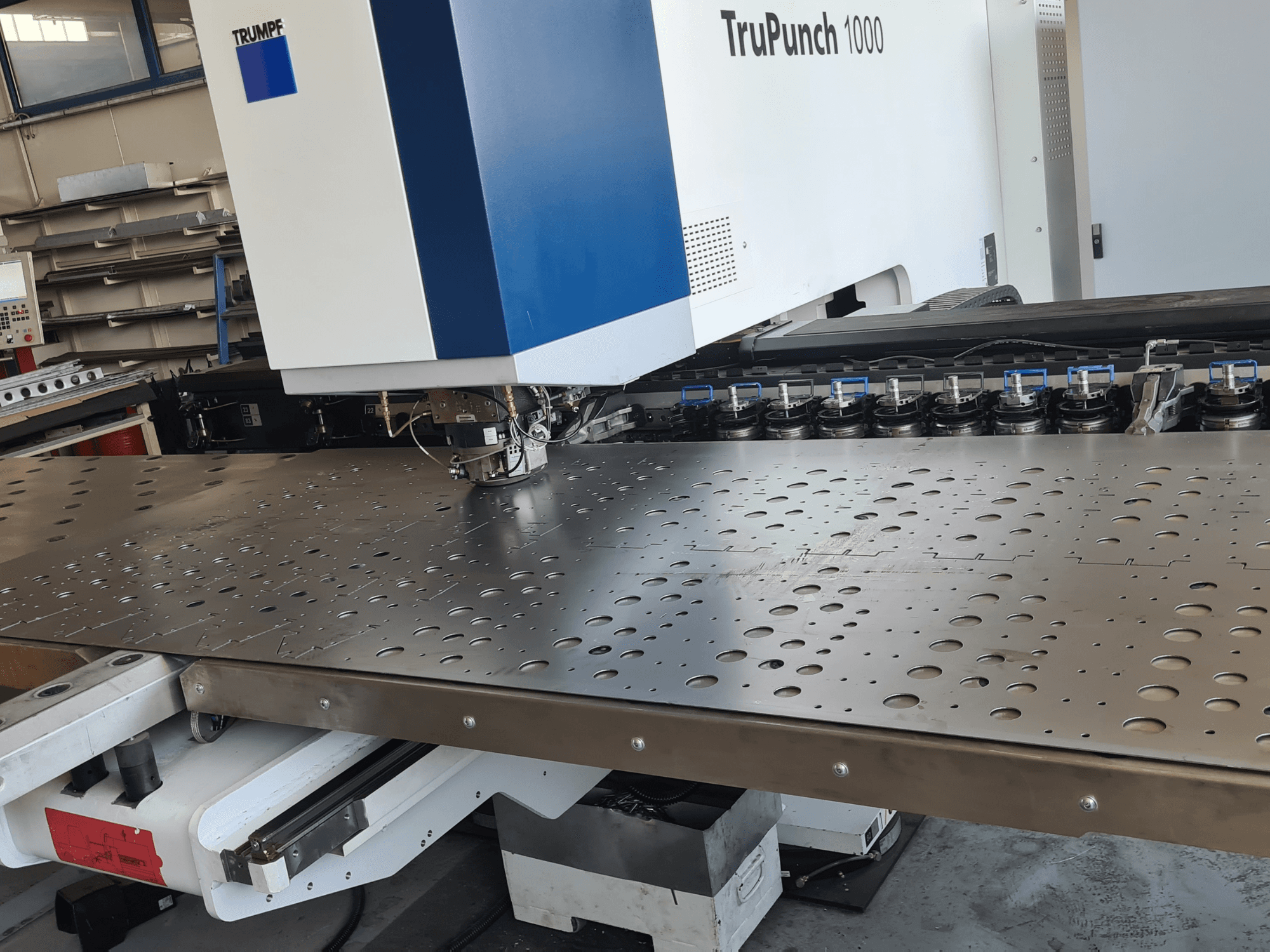 CNC-ponsmachine TRUMPF TruPunch 1000, vooraanzicht, met een geperforeerde metalen plaat en gereedschapsopstelling.