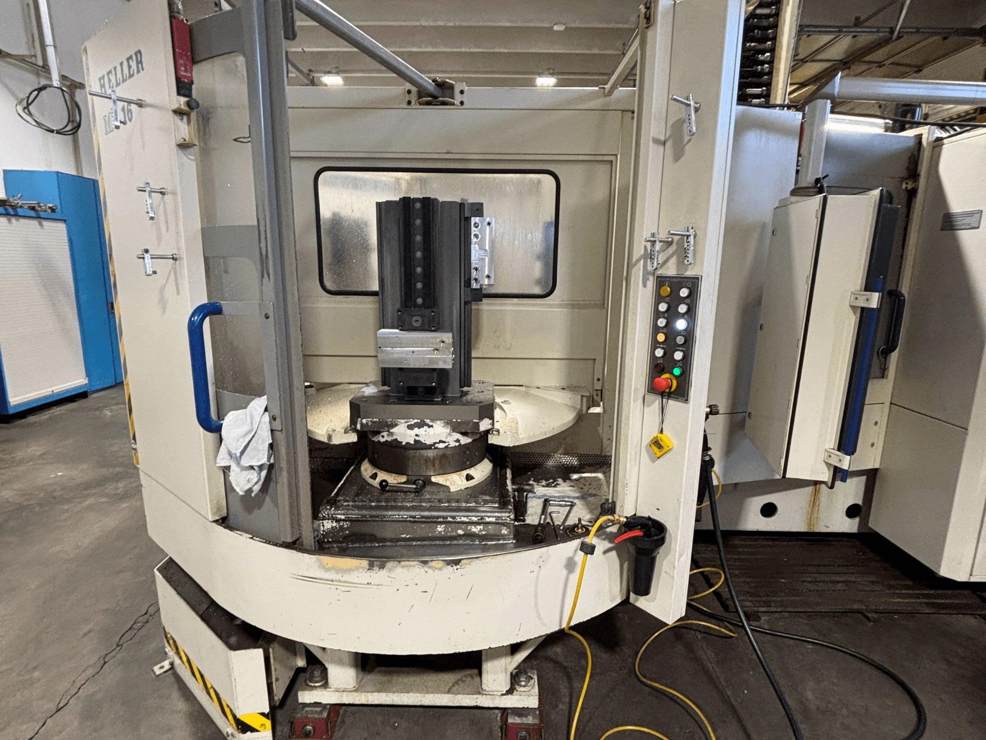 Heller bewerkingscentrum, model verticaal, vooraanzicht met spindel, bedieningspaneel en werktafel met aangesloten apparatuur.