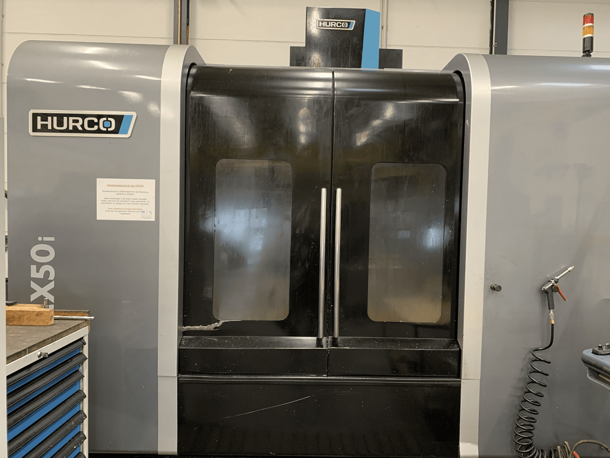 Vooraanzicht van een Hurco VX50i CNC machine met dubbele deuren, met technische bedieningselementen en een onderhoudsteken aan de zijkant.