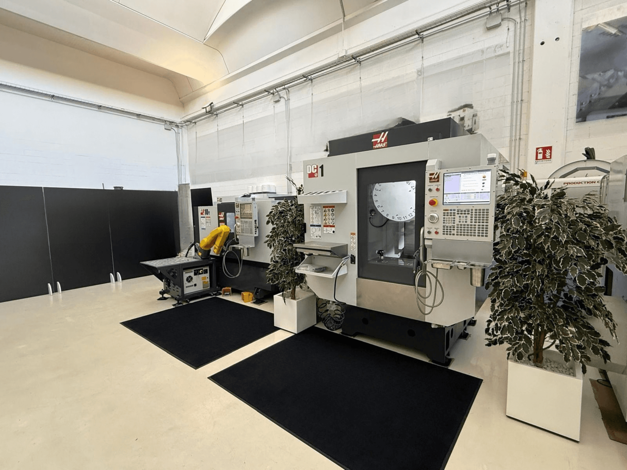 Vooraanzicht van een HAAS DC-1 verticaal bewerkingscentrum in een schone werkruimte, met een bedieningspaneel met touchscreen en de omliggende installaties.
