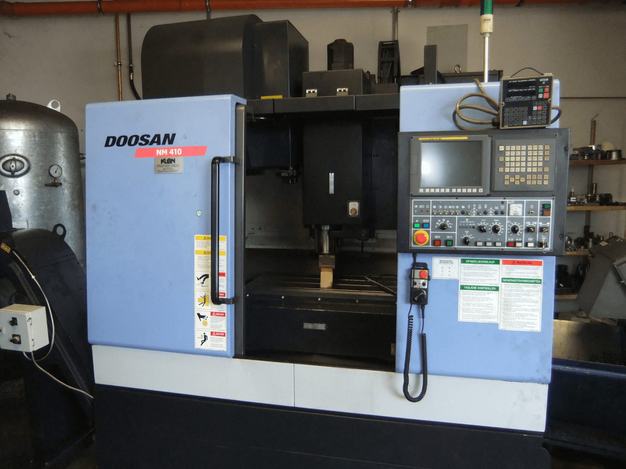 DOOSAN NM 410 verticaal bewerkingscentrum, vooraanzicht, met het bedieningspaneel, het spilgedeelte en de veiligheidslabels.
