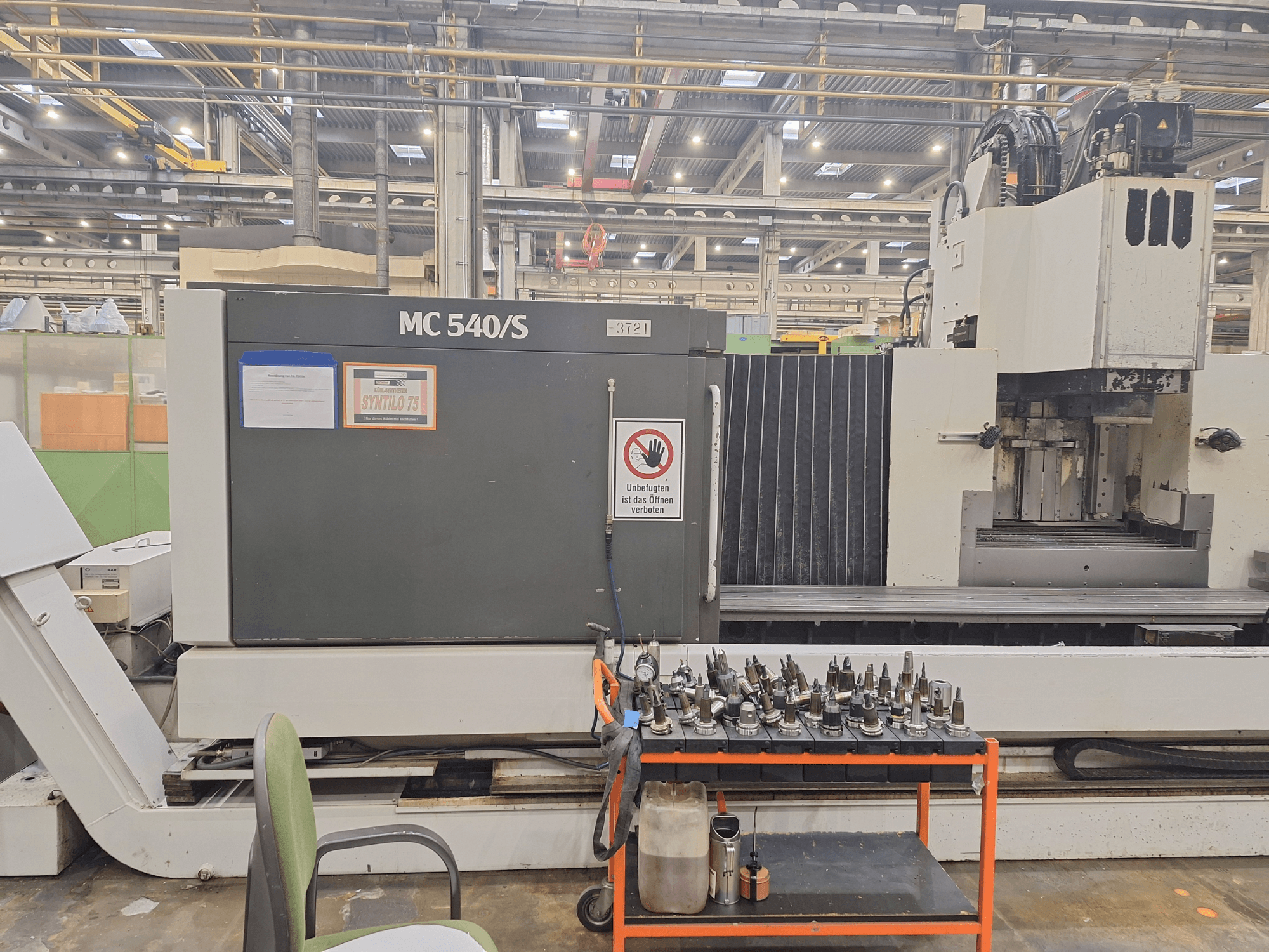 Verticaal bewerkingscentrum STAMA MC 540S in een werkplaats, zijaanzicht met gereedschaphouders op een kar vlakbij.