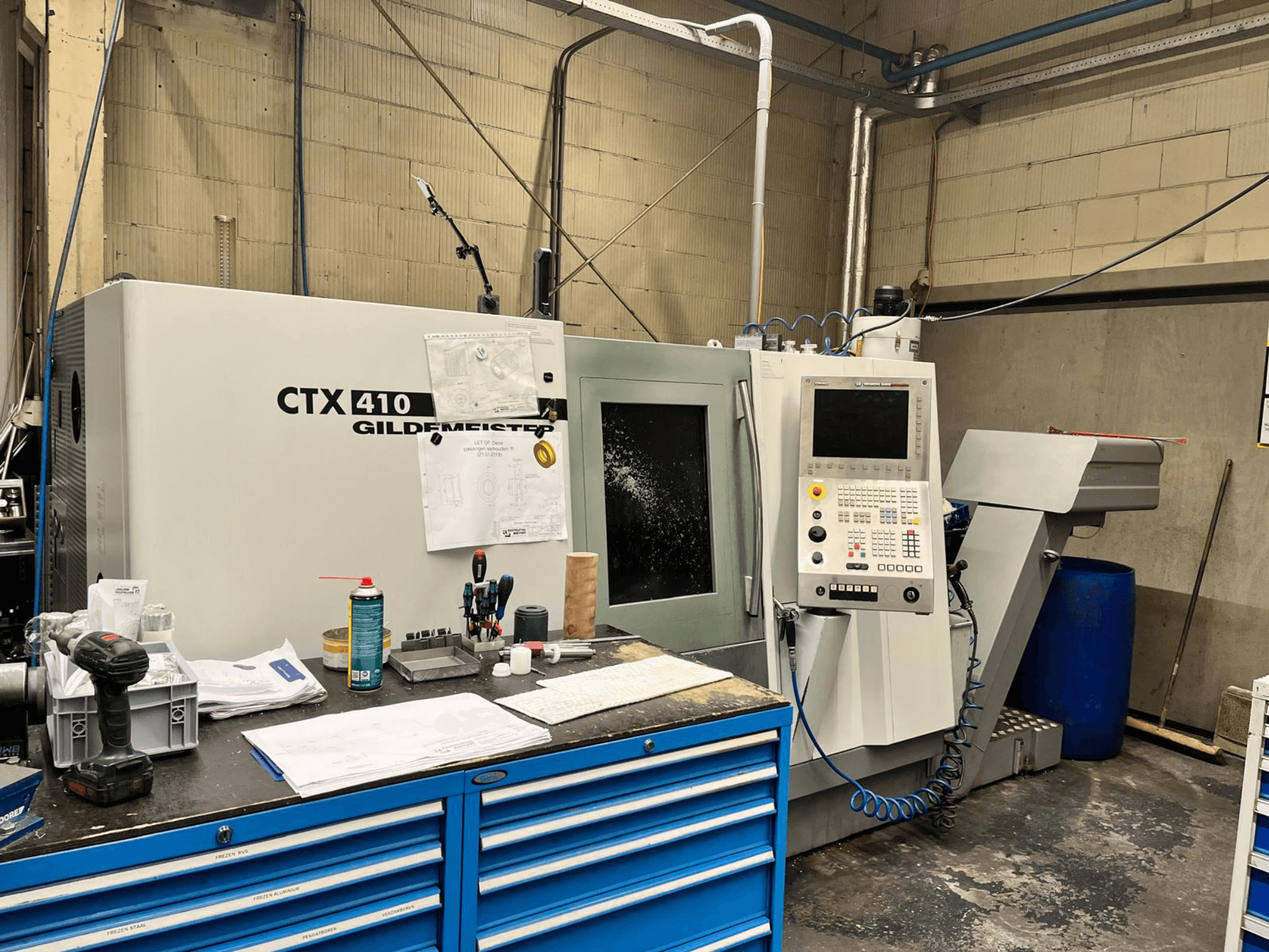 Gildemeister CTX 410 CNC machine in een werkplaats, vooraanzicht, met een bedieningspaneel en diverse gereedschappen op een werkbank.