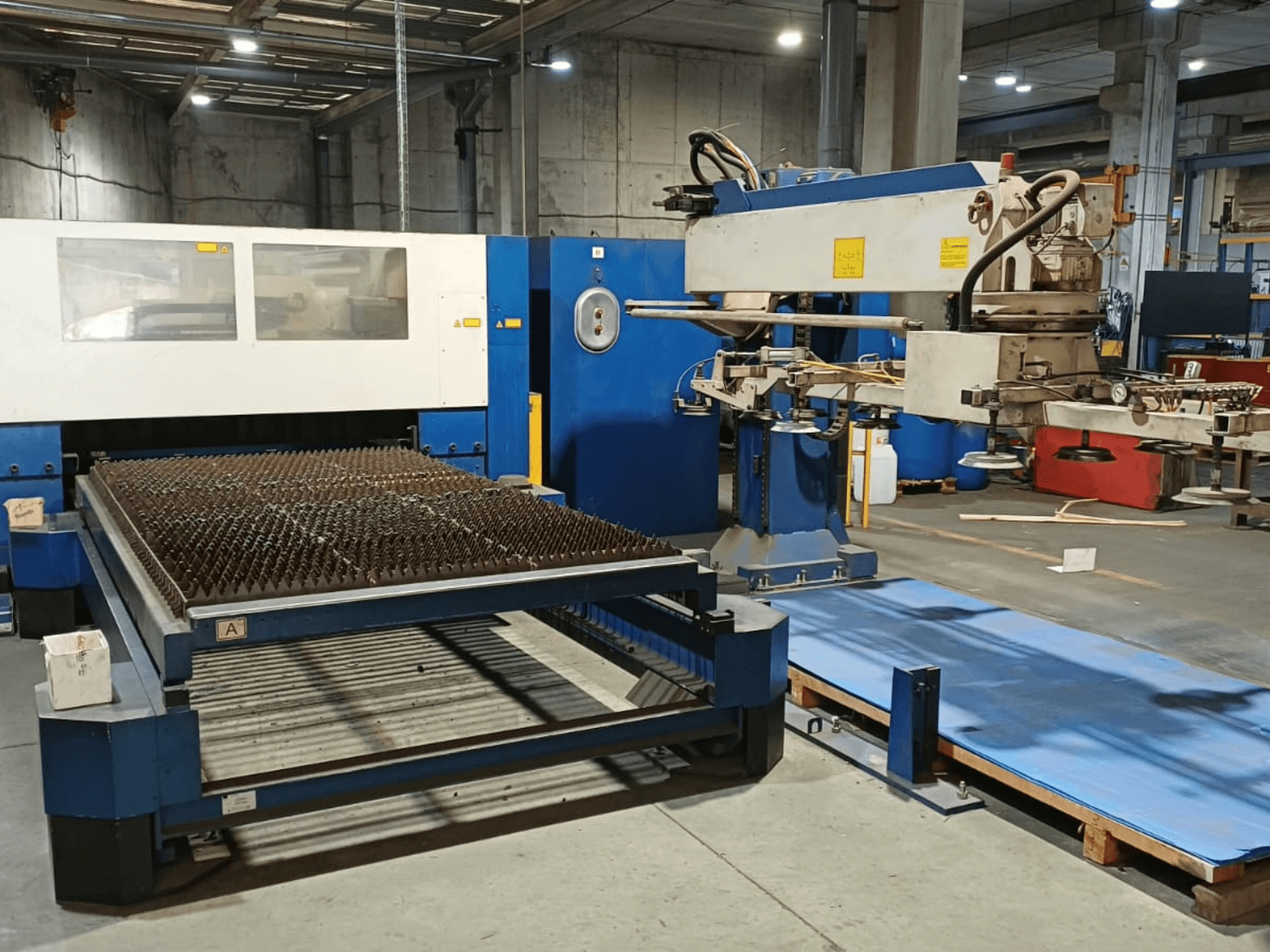 TRUMPF TRUMATIC L 3030 CO₂-lasersnijmachine, zijaanzicht, met de snijtafel met genopte oppervlak en de robotarm.