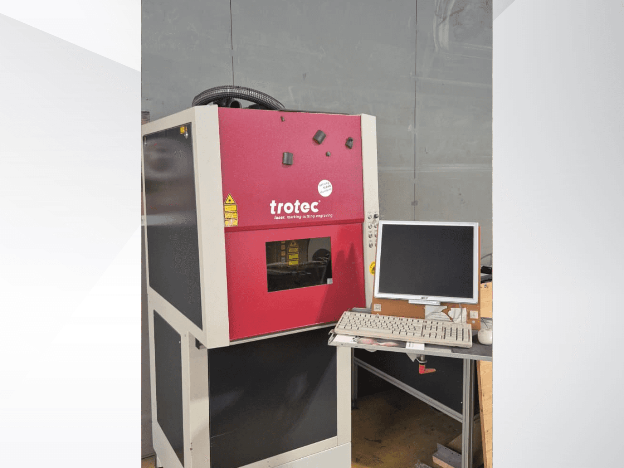 Rood Trotec-laserwerkstation, gezien vanaf de voorkant, met een monitor en toetsenbord op het werkstation.