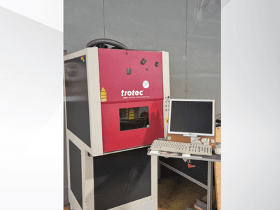 Rood Trotec-laserwerkstation, gezien vanaf de voorkant, met een monitor en toetsenbord op het werkstation.