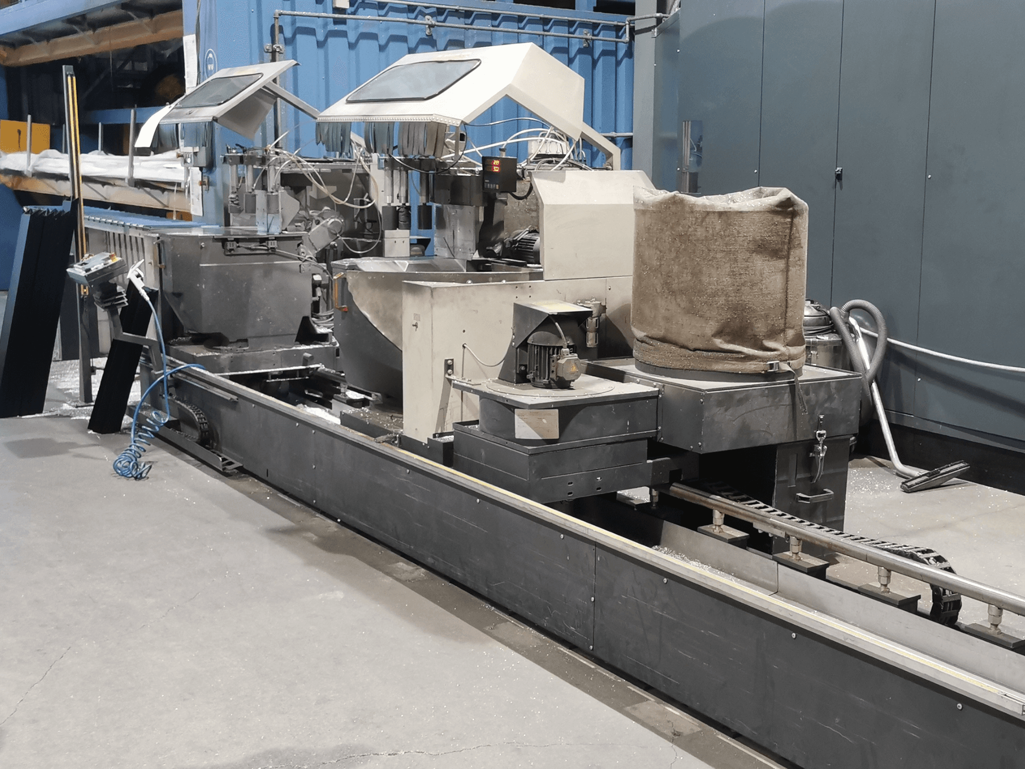 Industriële verwerkingsmachine gezien vanaf de zijkant, met trechters, transportband en bedieningspaneel, in een fabrieksomgeving.