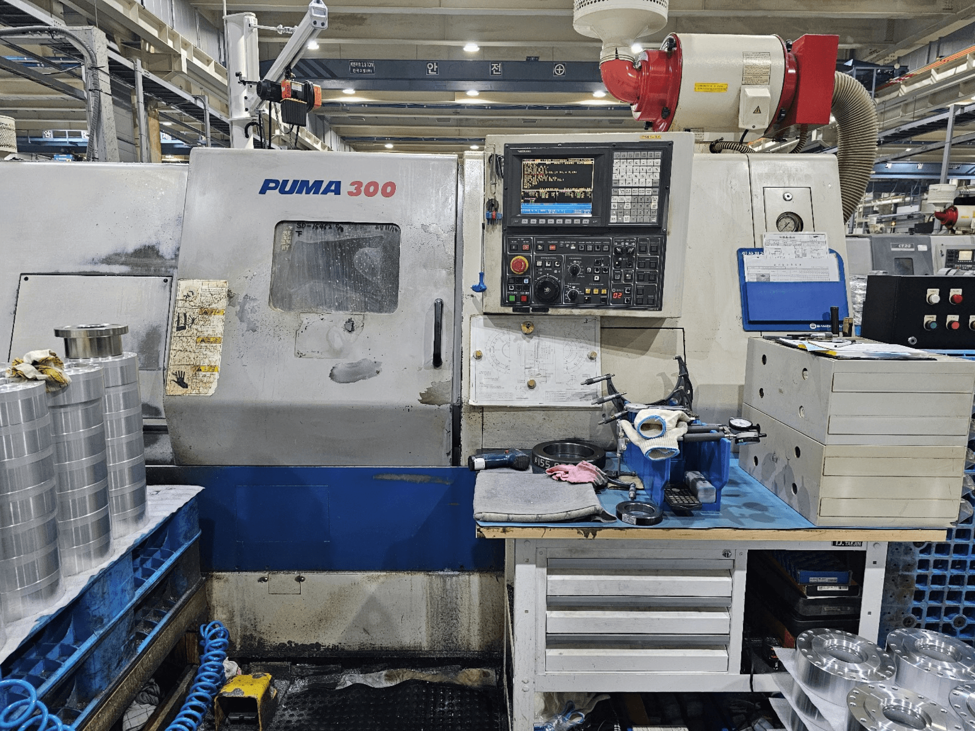 PUMA 300 CNC machine in een werkplaats; vooraanzicht met bedieningspaneel, gereedschappen en metalen onderdelen op een werkbank.