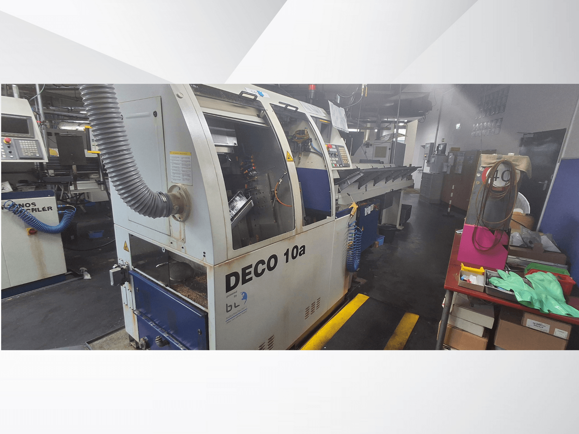 DECO 10a CNC machine in een werkplaats, vooraanzicht; voorzien van een bedieningspaneel en stofafzuigsysteem, met een werkbank ernaast.