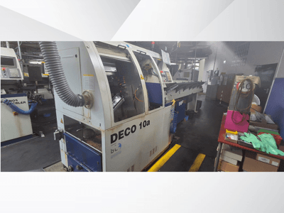 DECO 10a CNC machine in een werkplaats, vooraanzicht; voorzien van een bedieningspaneel en stofafzuigsysteem, met een werkbank ernaast.