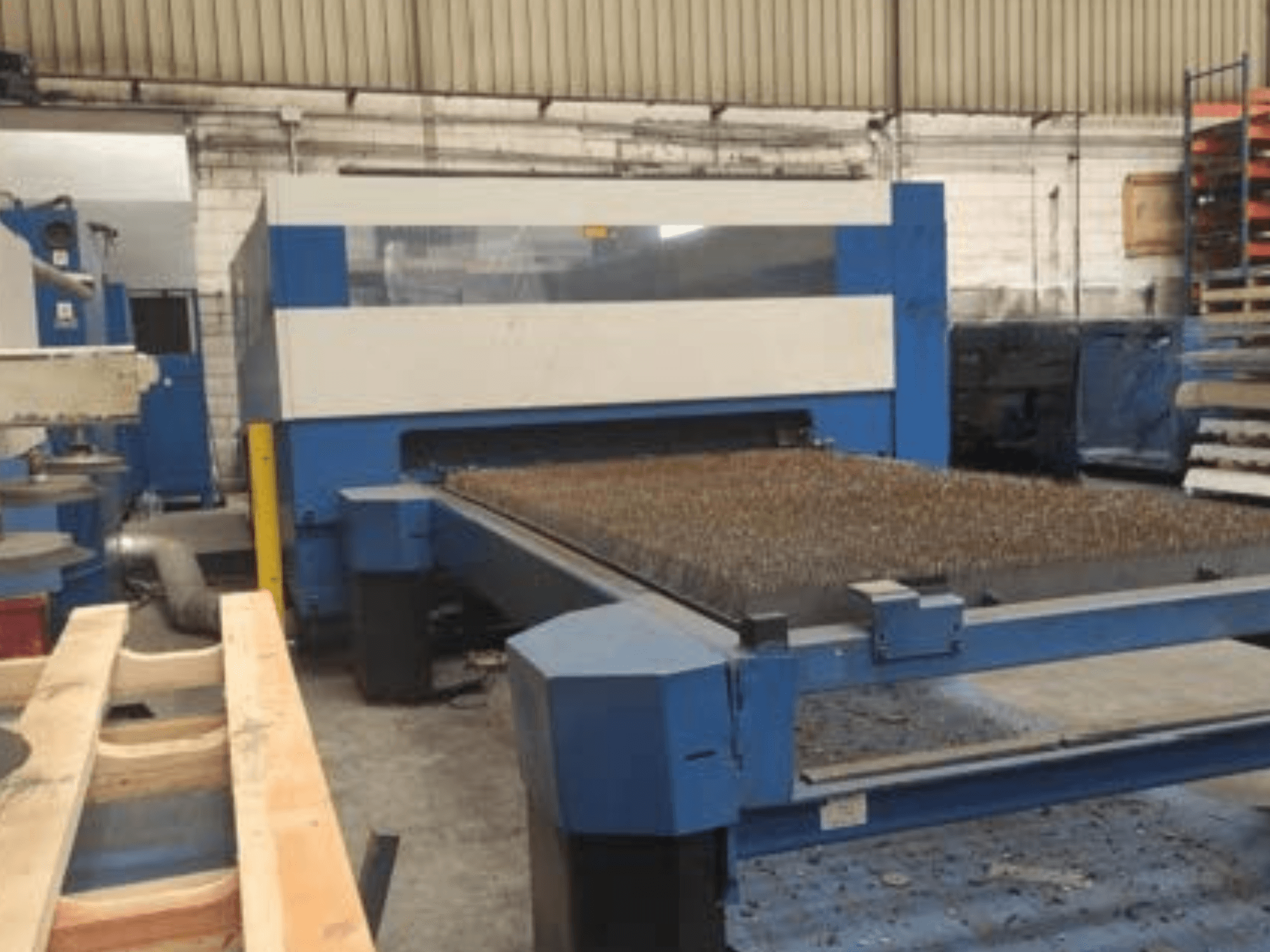 Blauwe lasersnijmachine met een metalen bed met structuur, zijaanzicht, toont de operationele opstelling in een industriële werkruimte.