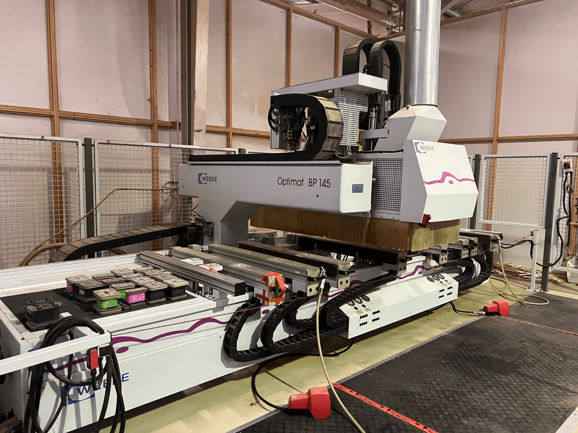 WEEKE Optimat BP 145 in een fabriek, met een CNC machine met bedieningsknoppen en kabels, gezien vanaf de zijkant.