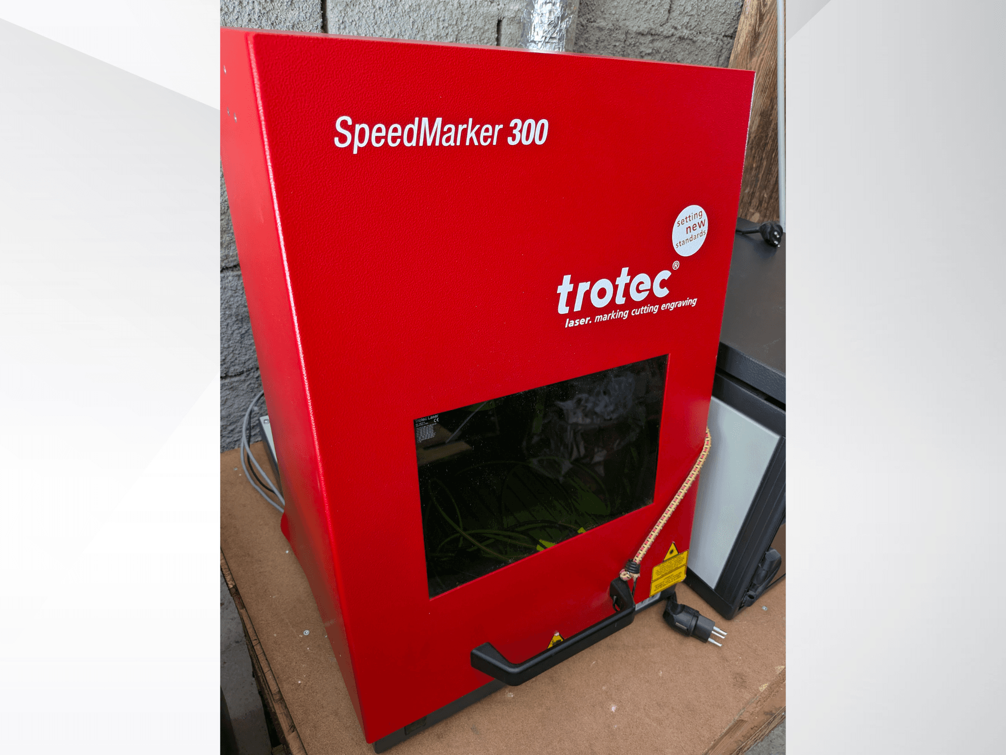 Rode Trotec SpeedMarker 300 lasermarkeermachine in vooraanzicht, met een groot kijkvenster en stroomaansluiting.